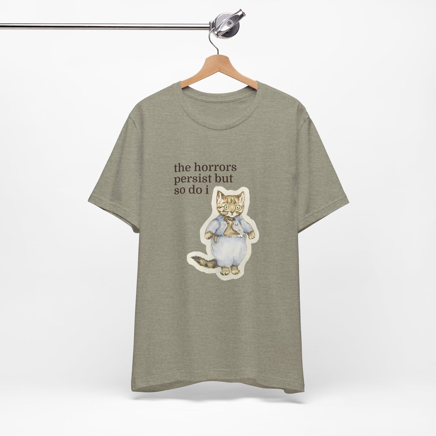 Green t-shirt featuring a vintage-style illustrated cat in blue clothing with the phrase “the horrors persist but so do i.”