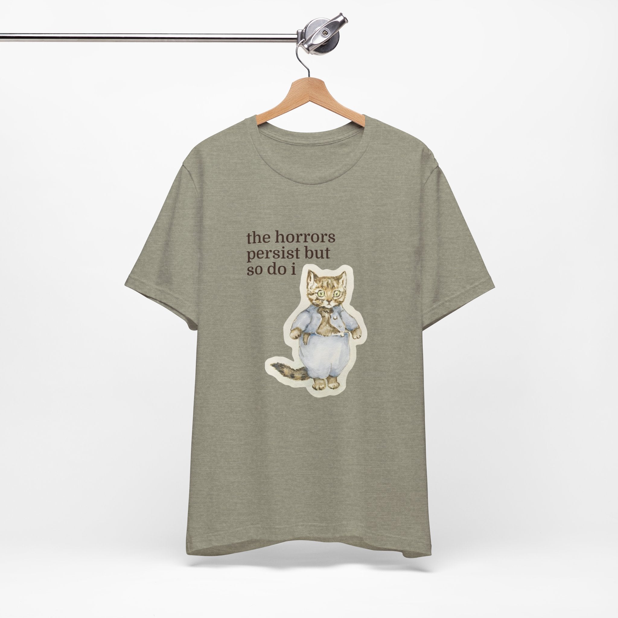Green t-shirt featuring a vintage-style illustrated cat in blue clothing with the phrase “the horrors persist but so do i.”