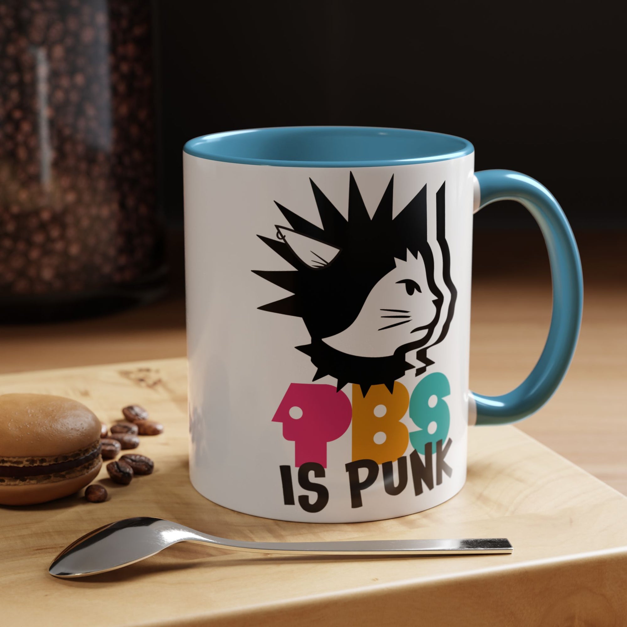 Mug with a colorful design and text on a wooden surface with coffee beans and a spoon.