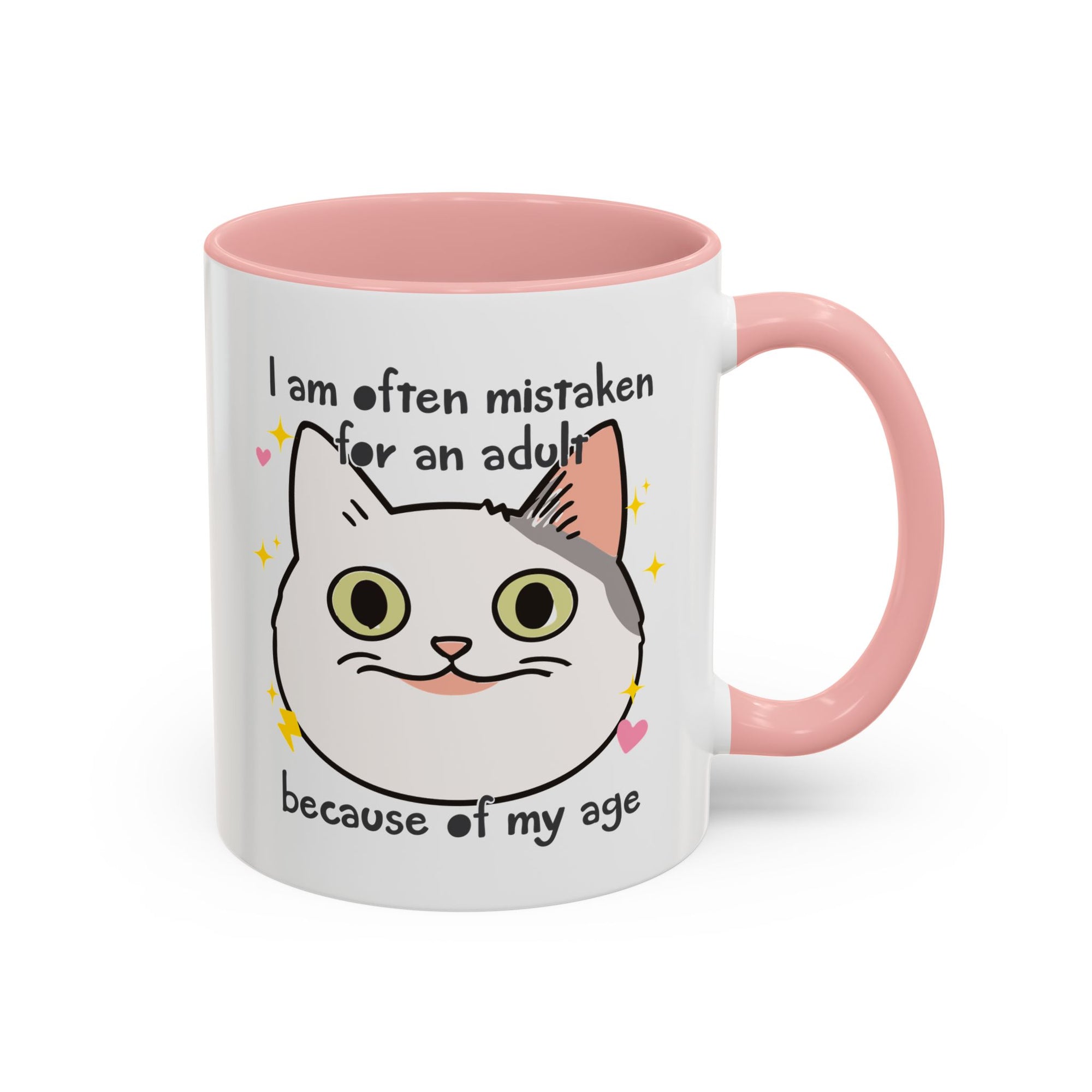 White ceramic mug with peach handle and interior featuring a cute wide-eyed cat face, hearts, sparkles, and the phrase “I am often mistaken for an adult because of my age.”
