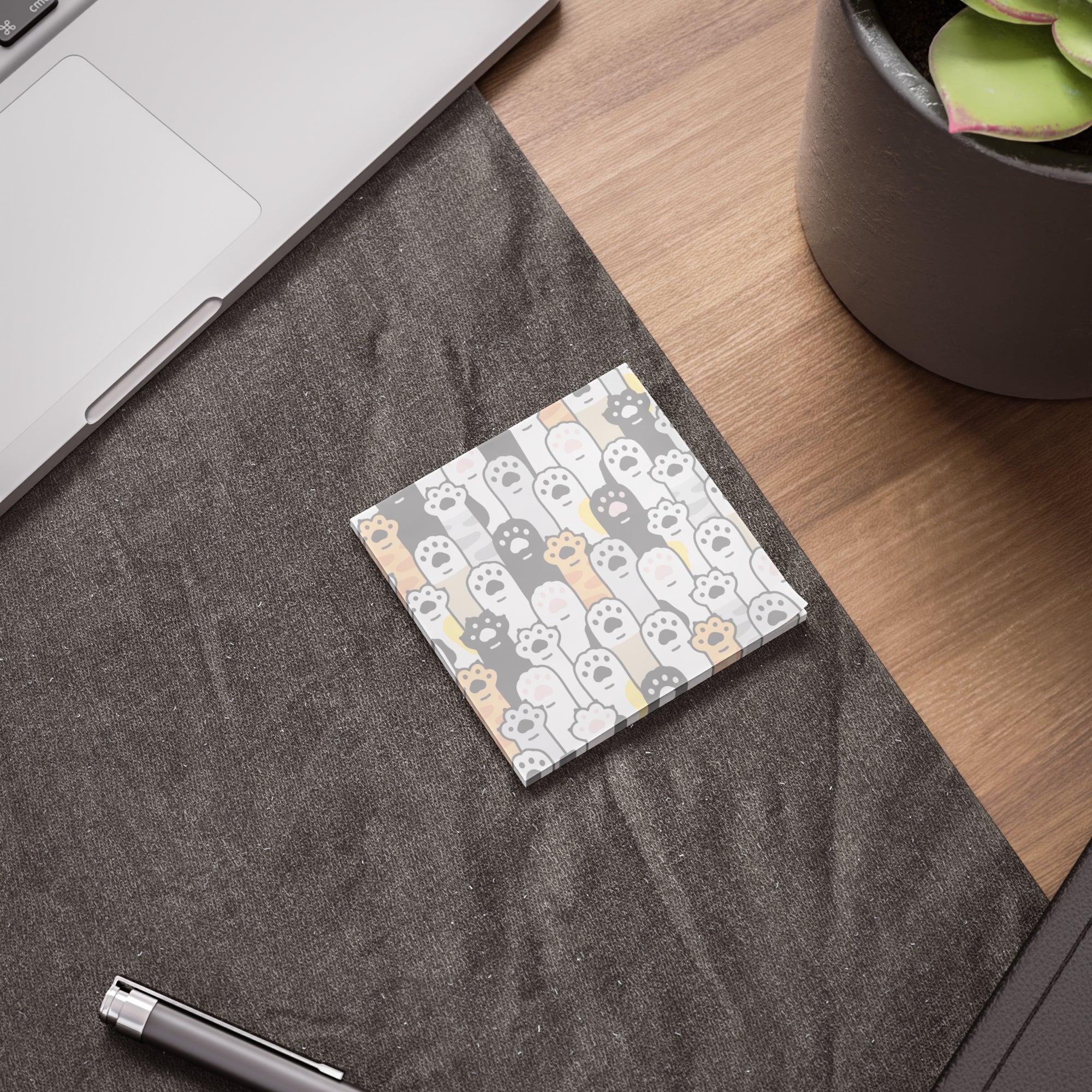 Post it notes with cat paws on a textured surface with a pen and plant in the background