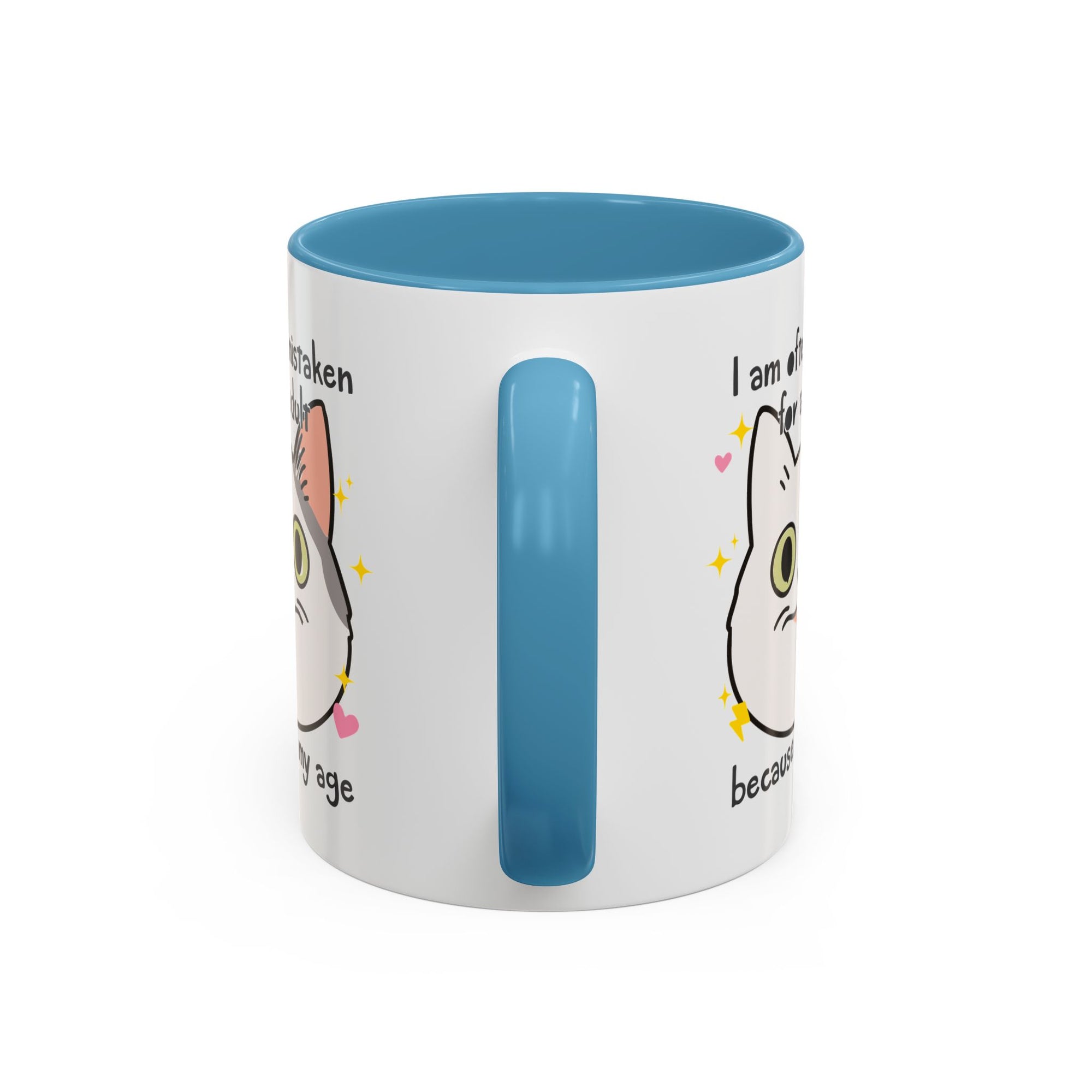 White ceramic mug with blue handle and interior featuring a cute wide-eyed cat face, hearts, sparkles, and the phrase “I am often mistaken for an adult because of my age.”
