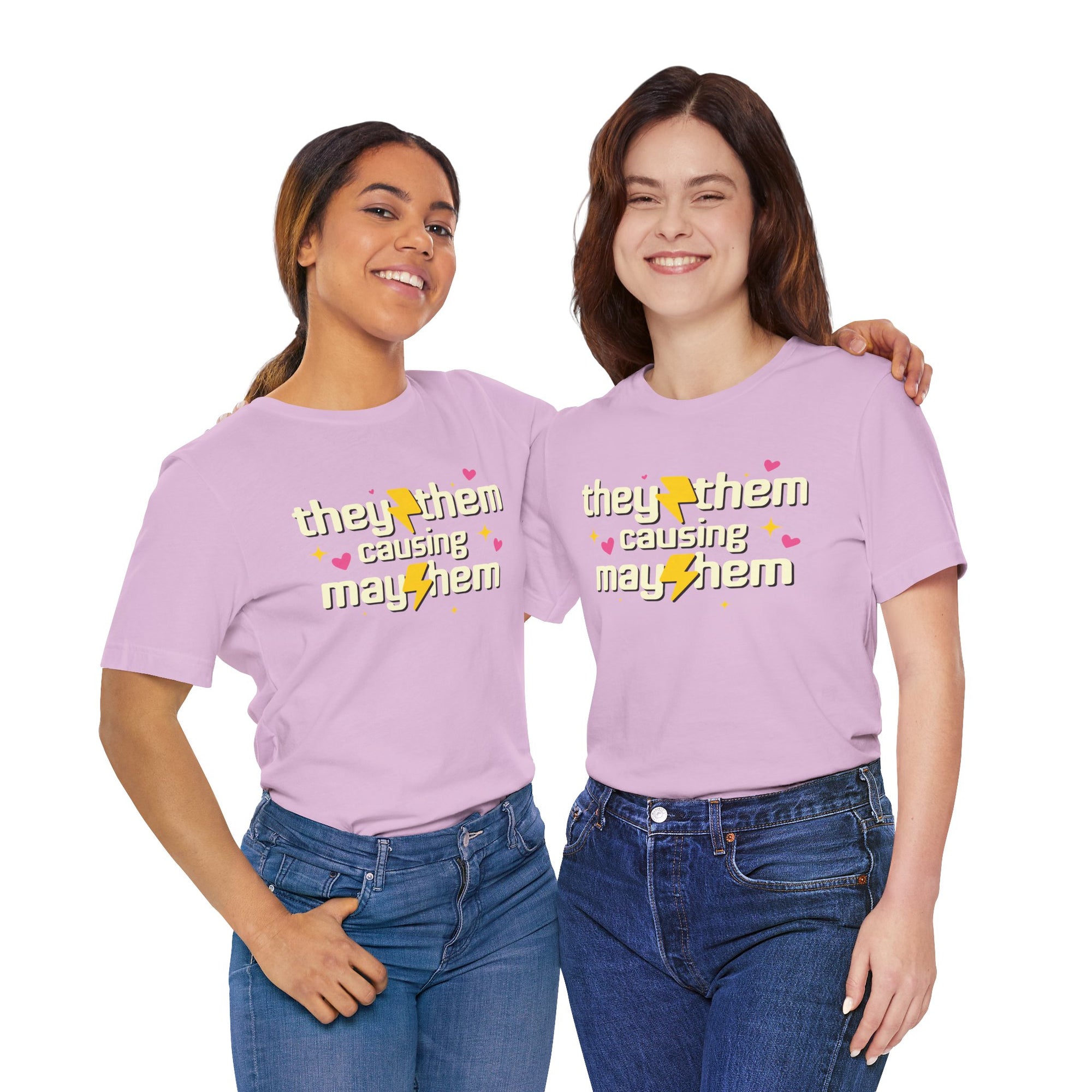 pink t-shirt featuring the phrase “They/Them Causing Mayhem” in retro-style lettering with yellow lightning bolts, pink hearts, and sparkle accents.
