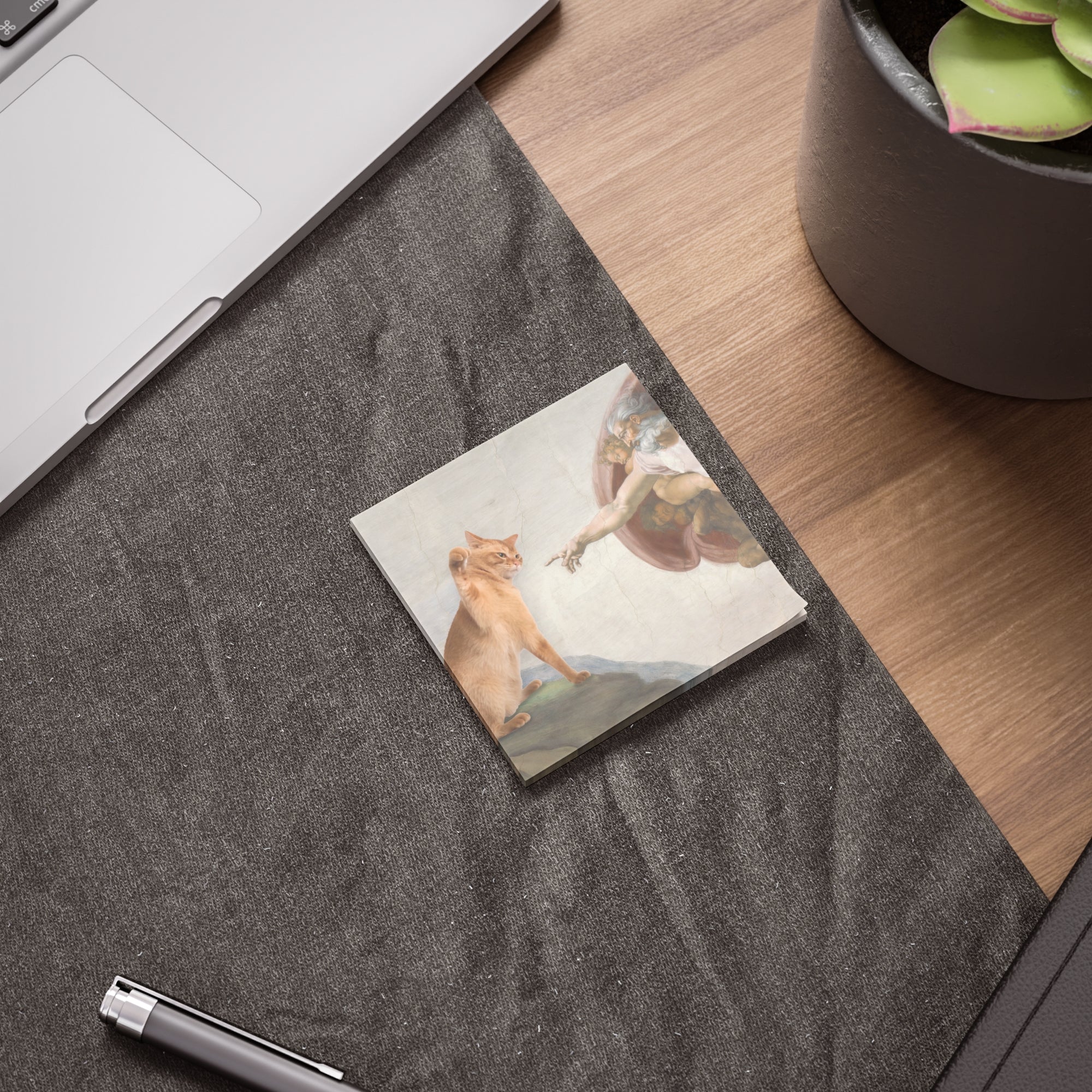 Notebook with a cat illustration on a desk next to a laptop and plant