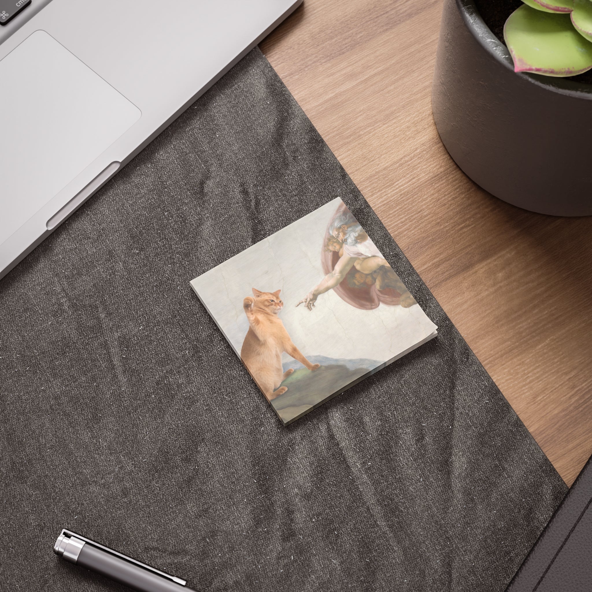 Notebook with a cat illustration on a desk next to a laptop and plant