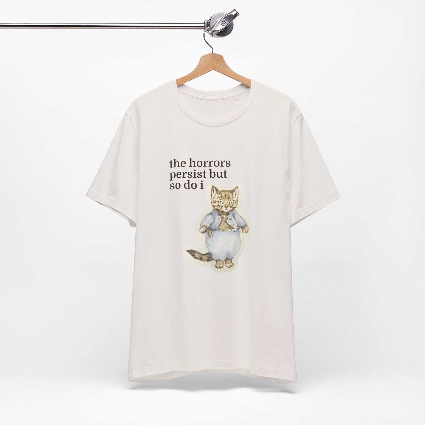 White t-shirt featuring a vintage-style illustrated cat in blue clothing with the phrase “the horrors persist but so do i.”