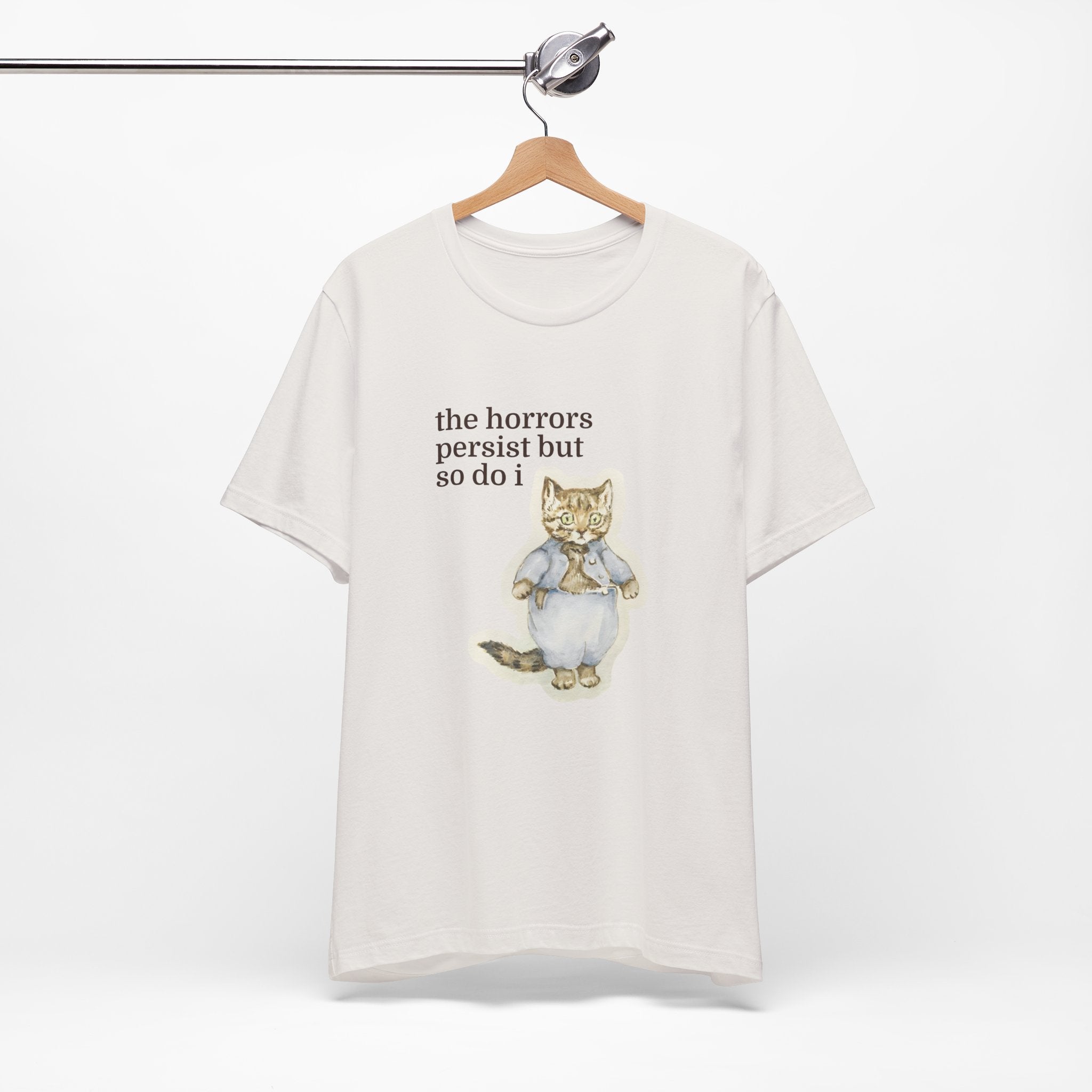White t-shirt featuring a vintage-style illustrated cat in blue clothing with the phrase “the horrors persist but so do i.”