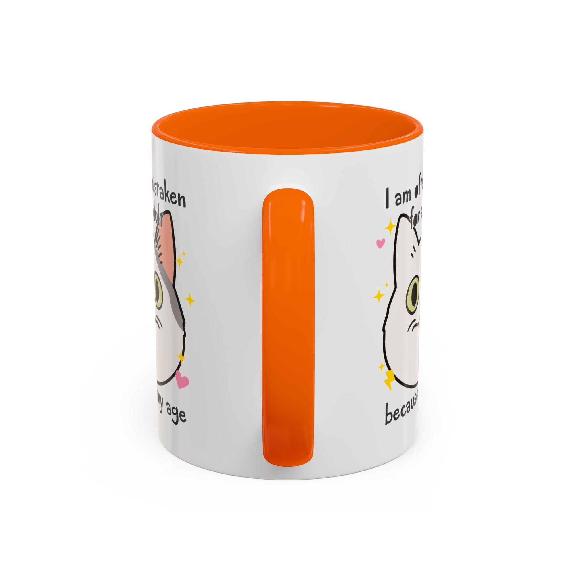 White ceramic mug with orange handle and interior featuring a cute wide-eyed cat face, hearts, sparkles, and the phrase “I am often mistaken for an adult because of my age.”
