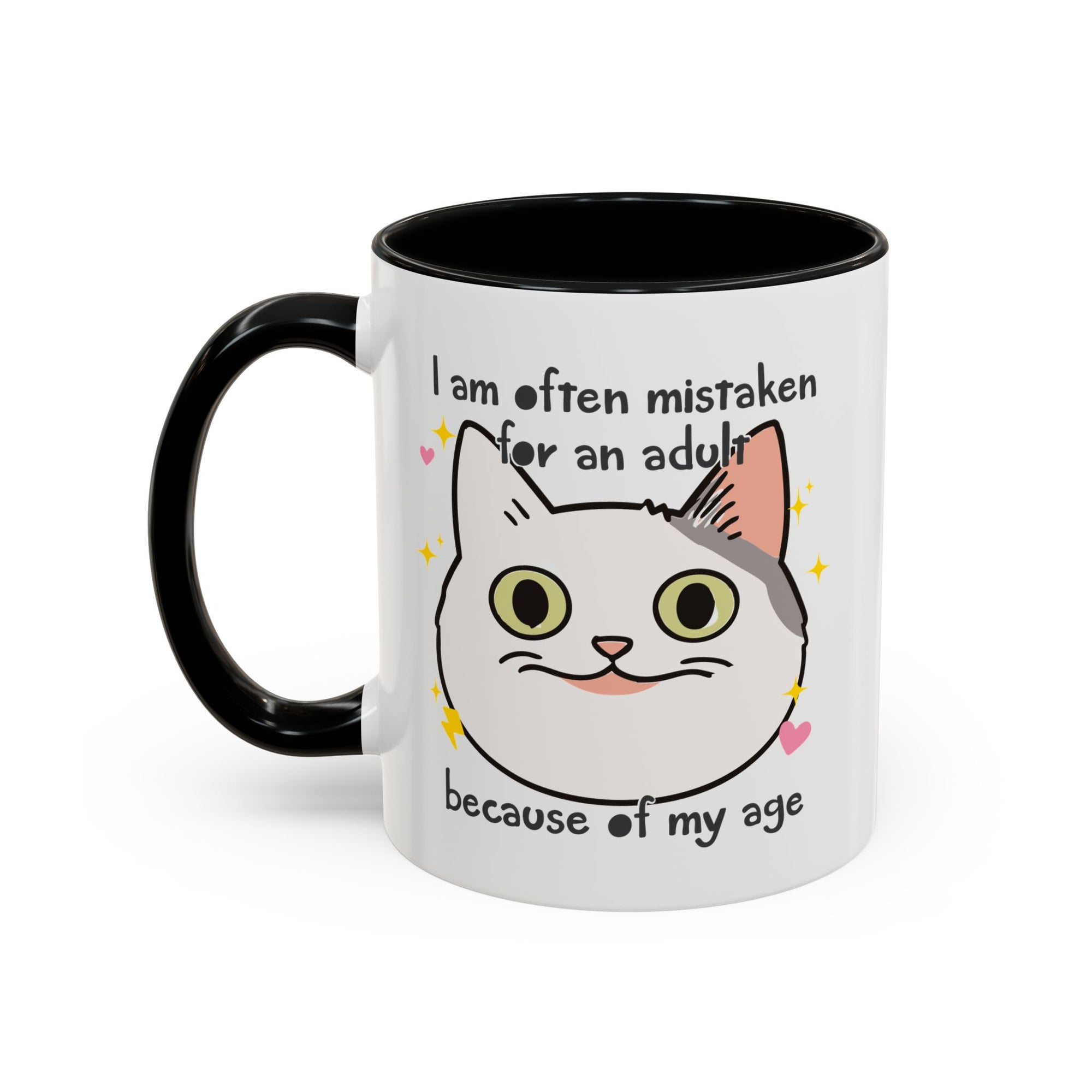 White ceramic mug with black handle and interior featuring a cute wide-eyed cat face, hearts, sparkles, and the phrase “I am often mistaken for an adult because of my age.”
