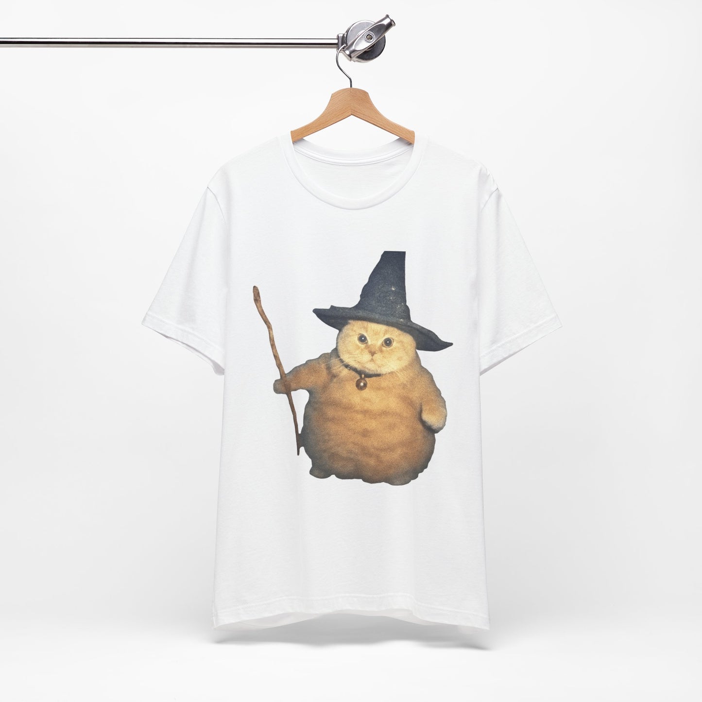 White t-shirt with a cat wearing a witch hat and broomstick design on a hanger.