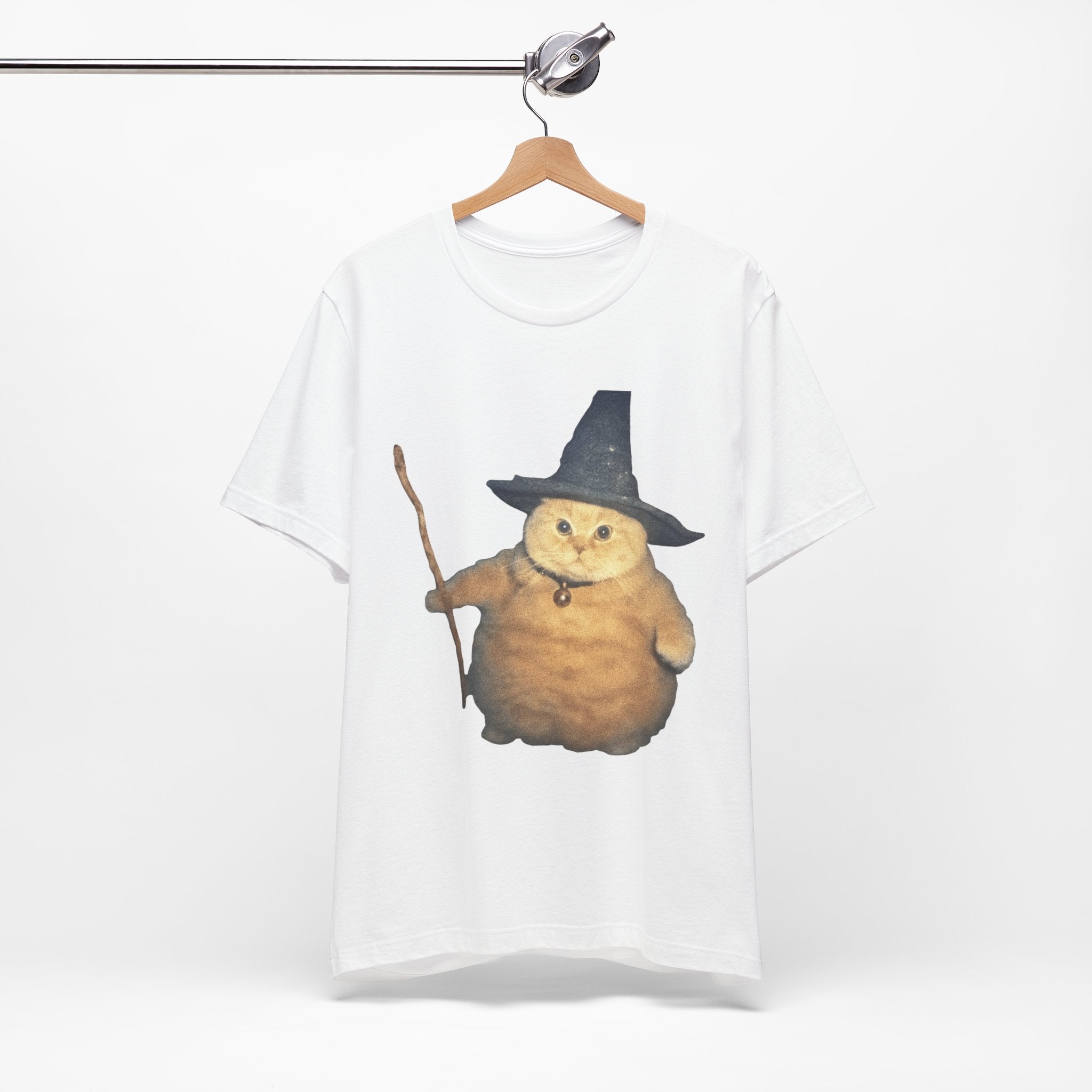 White t-shirt with a cat wearing a witch hat and broomstick design on a hanger.