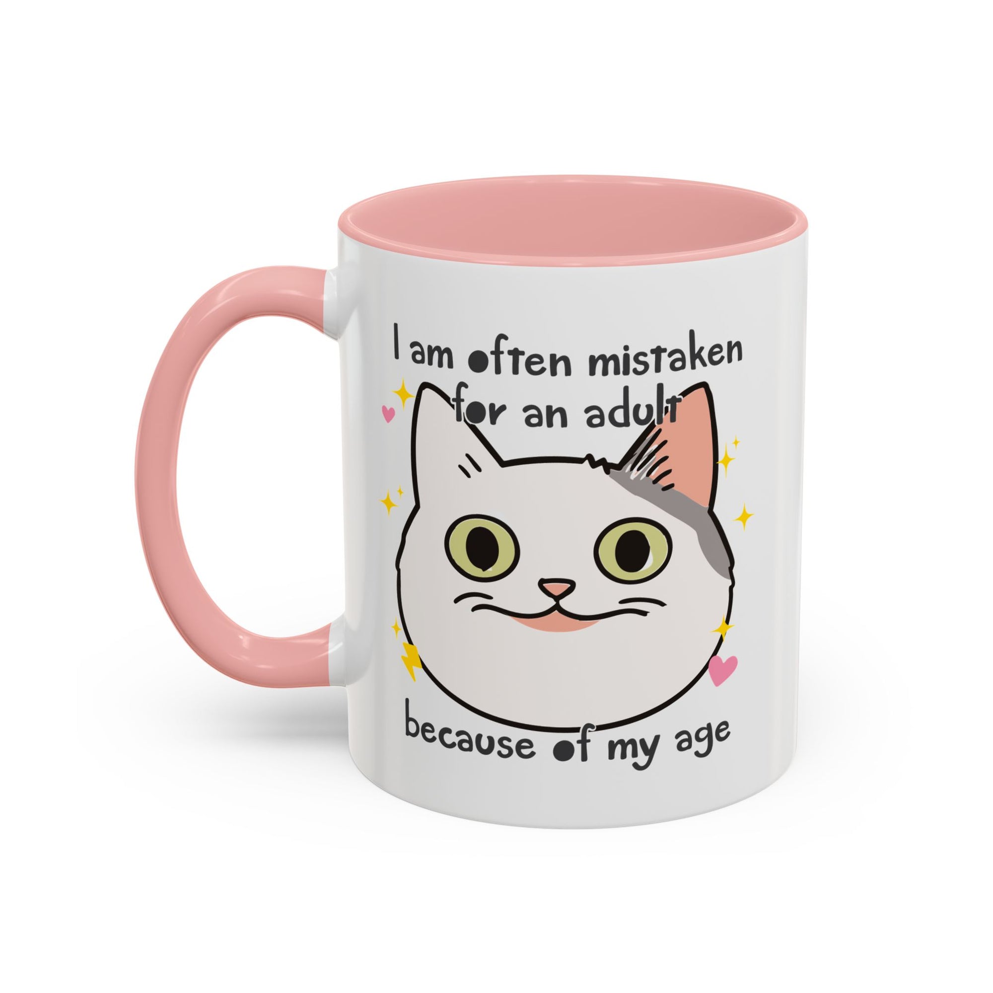 White ceramic mug with peach handle and interior featuring a cute wide-eyed cat face, hearts, sparkles, and the phrase “I am often mistaken for an adult because of my age.”
