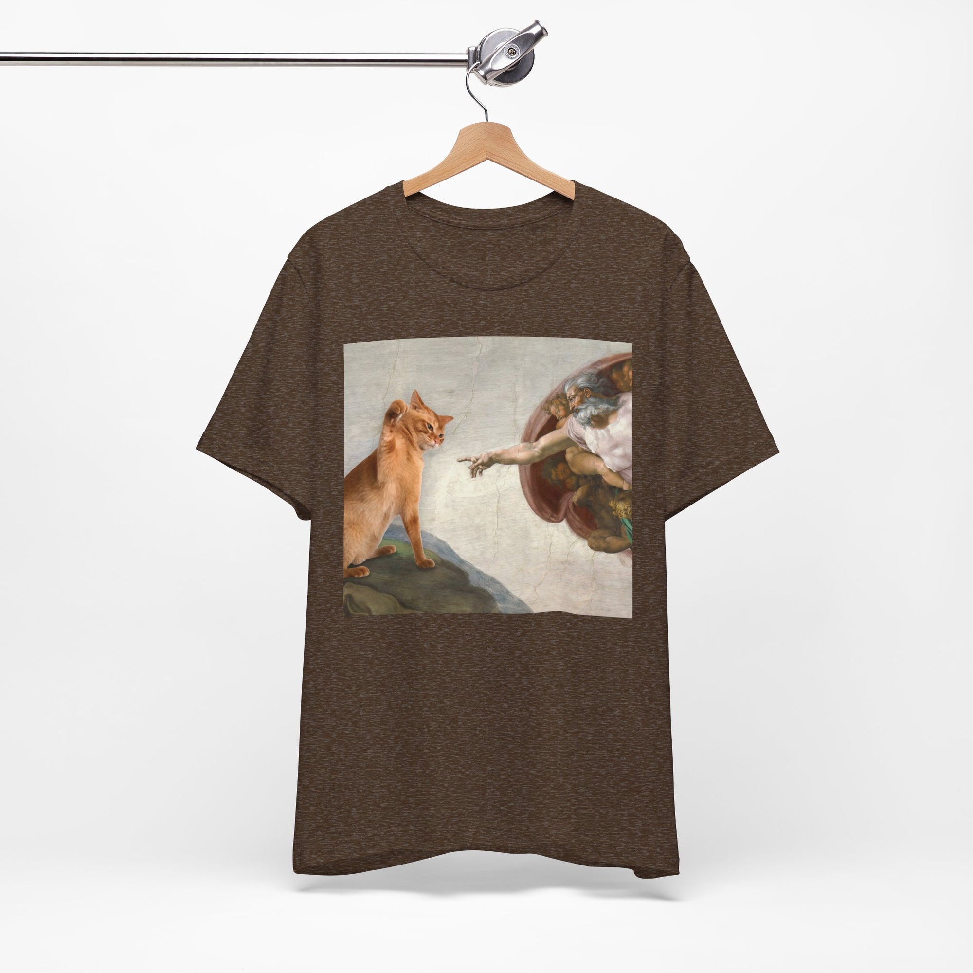 Brown t-shirt with a graphic design of a cat and angel on a hanger against a white background