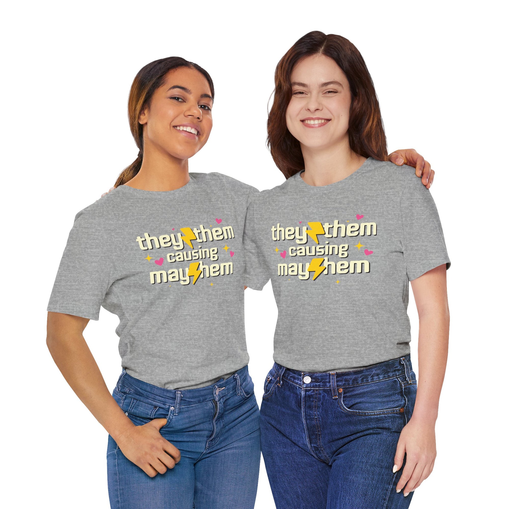 grey  t-shirt featuring the phrase “They/Them Causing Mayhem” in retro-style lettering with yellow lightning bolts, pink hearts, and sparkle accents.
