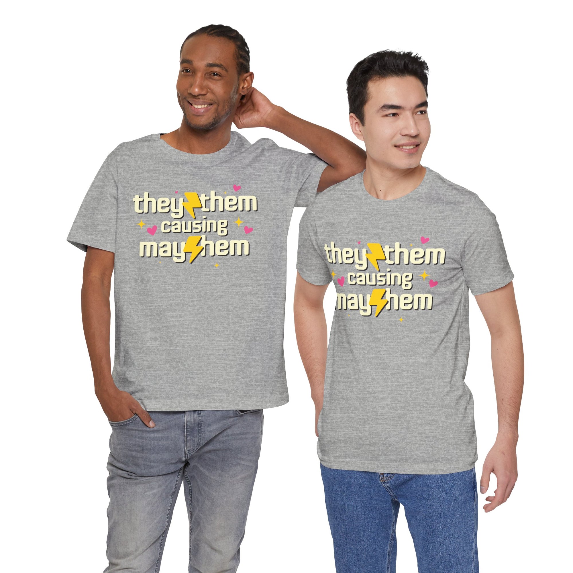 grey t-shirt featuring the phrase “They/Them Causing Mayhem” in retro-style lettering with yellow lightning bolts, pink hearts, and sparkle accents.
