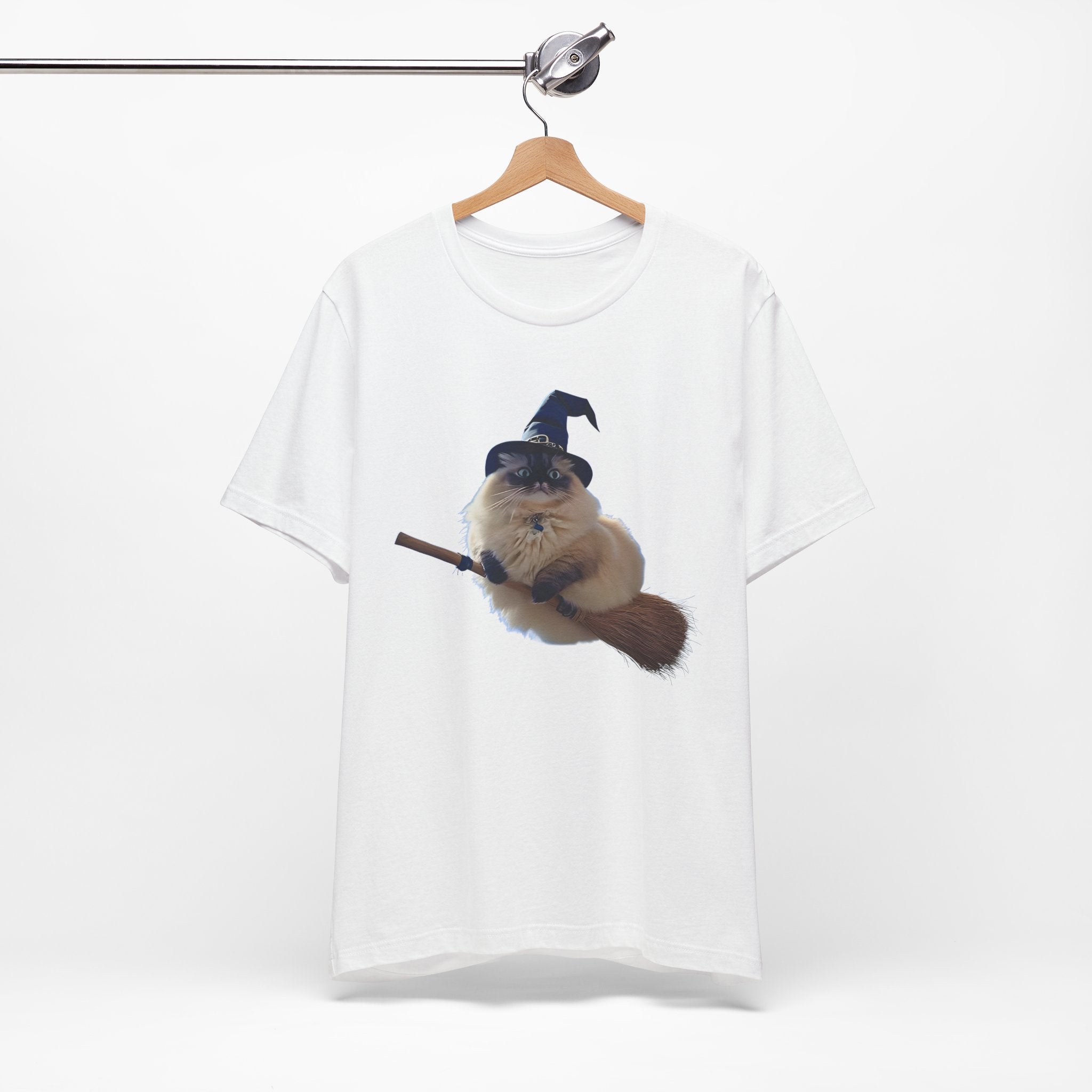 White t-shirt with a graphic of a cat wearing a witch hat and holding a broomstick, hanging on a wooden hanger against a white background.