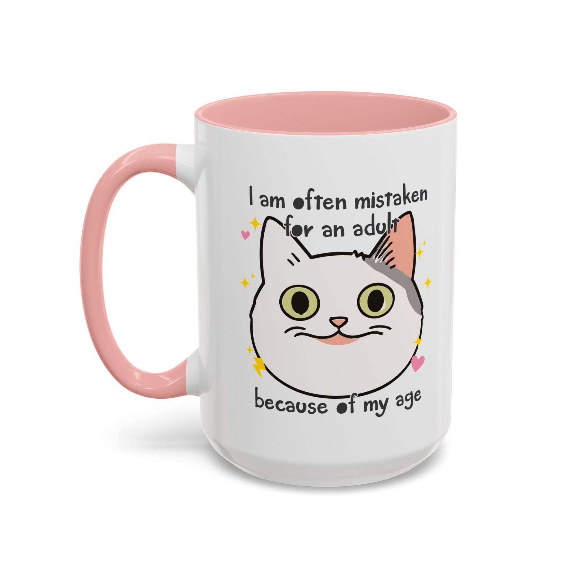 White ceramic mug with peach handle and interior featuring a cute wide-eyed cat face, hearts, sparkles, and the phrase “I am often mistaken for an adult because of my age.”
