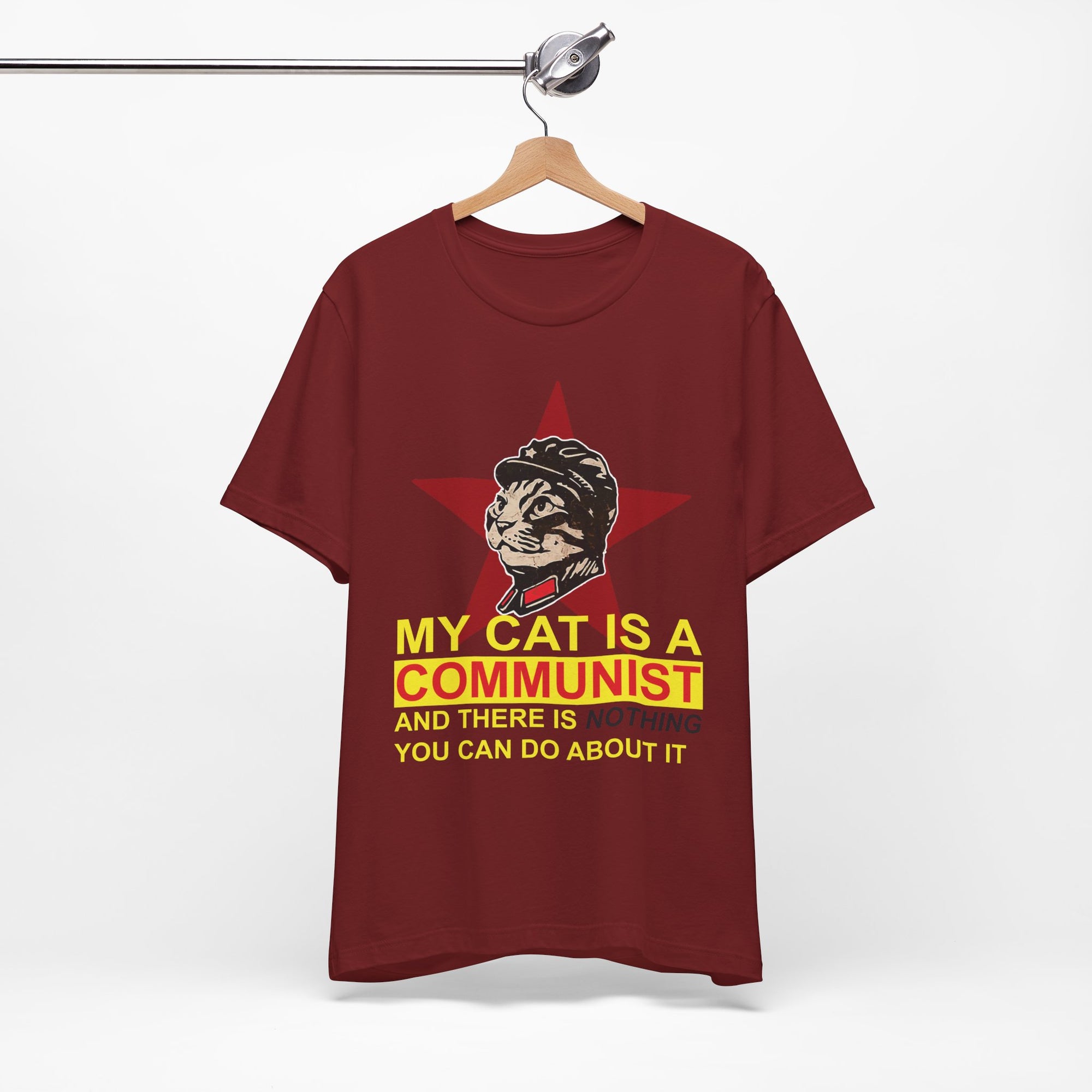 Maroon t-shirt with a graphic of a cat in a helmet and text on a hanger against a white background