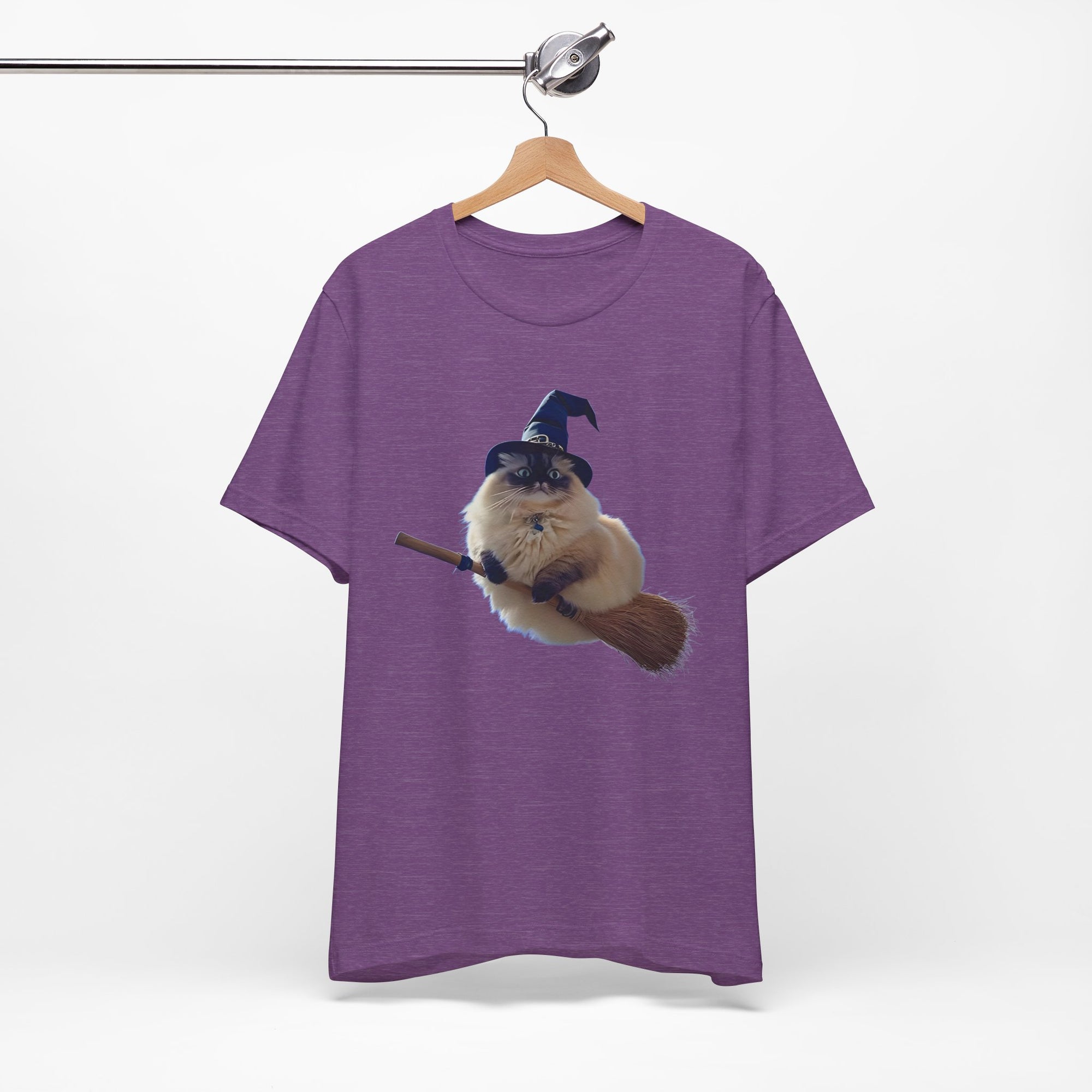 Purple t-shirt with a graphic of a cat in a wizard hat and broom on a hanger against a white background