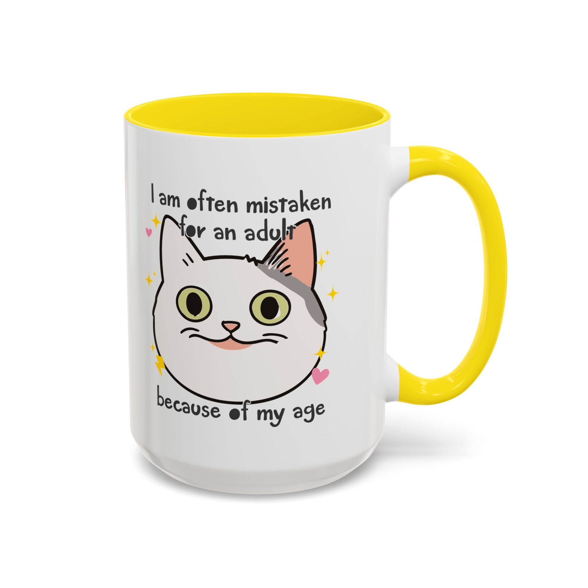 White ceramic mug with yellow  handle and interior featuring a cute wide-eyed cat face, hearts, sparkles, and the phrase “I am often mistaken for an adult because of my age.”
