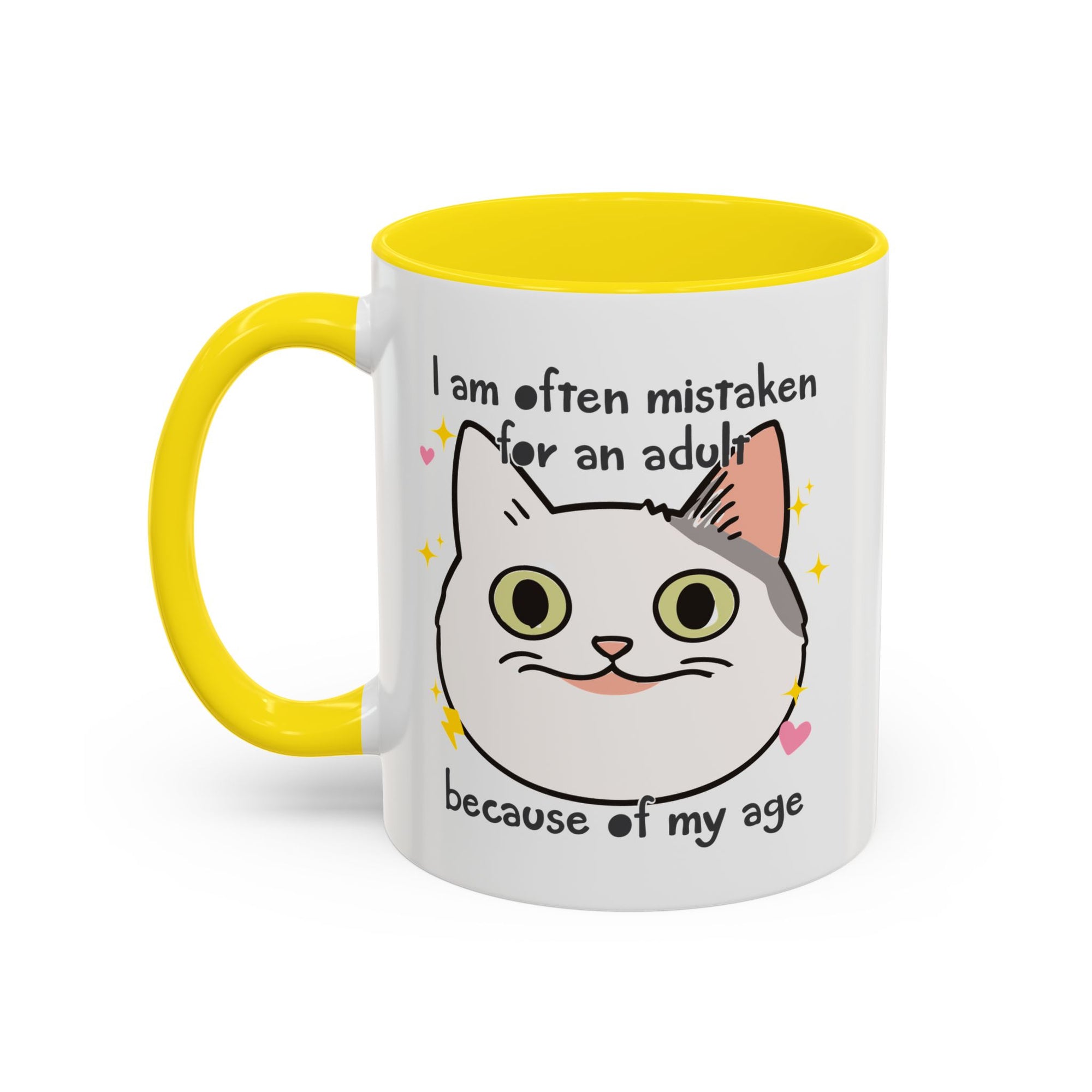 White ceramic mug with yellow handle and interior featuring a cute wide-eyed cat face, hearts, sparkles, and the phrase “I am often mistaken for an adult because of my age.”
