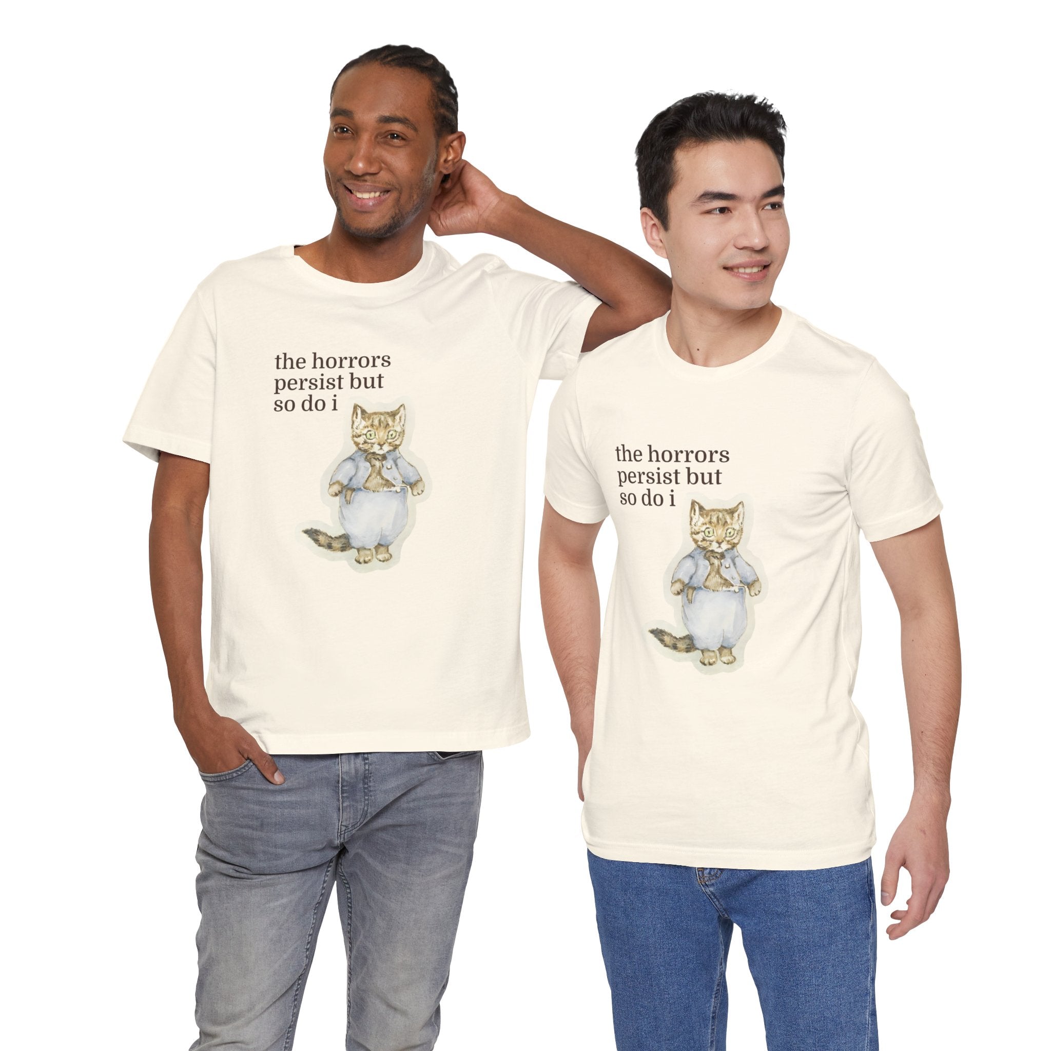 Two men wearing cream t-shirt featuring a vintage-style illustrated cat in blue clothing with the phrase “the horrors persist but so do i.”
