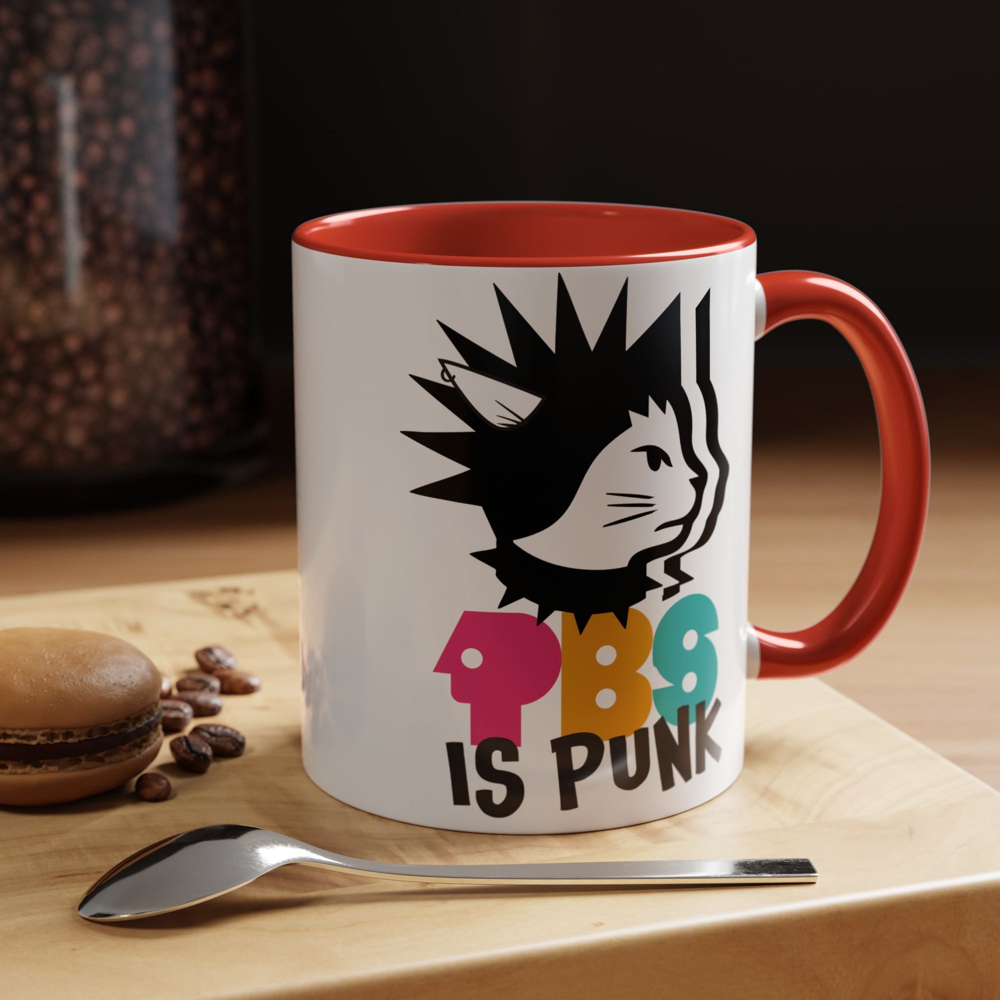 Mug with colorful design and text on a wooden surface with coffee beans and a spoon.