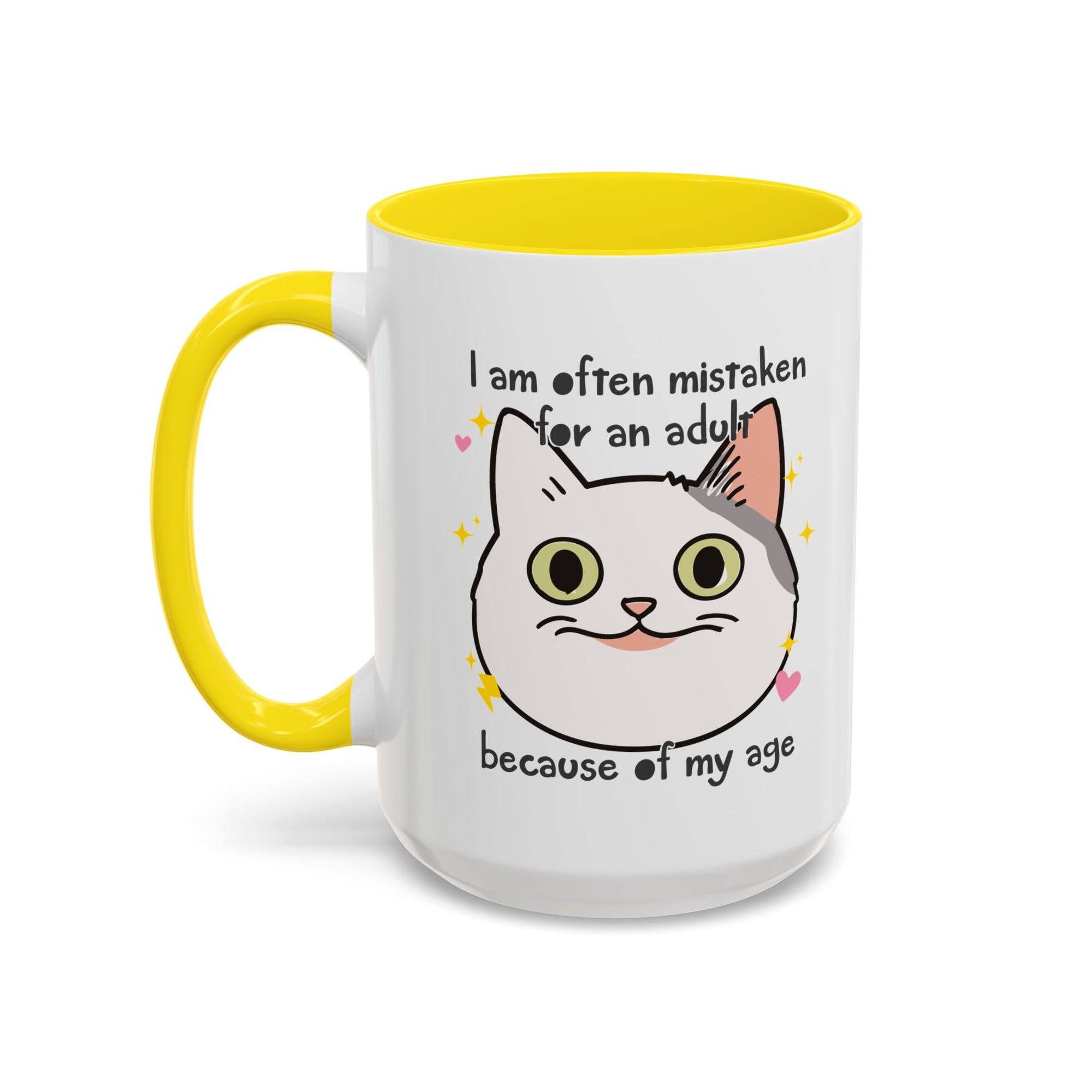 White ceramic mug with yellow handle and interior featuring a cute wide-eyed cat face, hearts, sparkles, and the phrase “I am often mistaken for an adult because of my age.”
