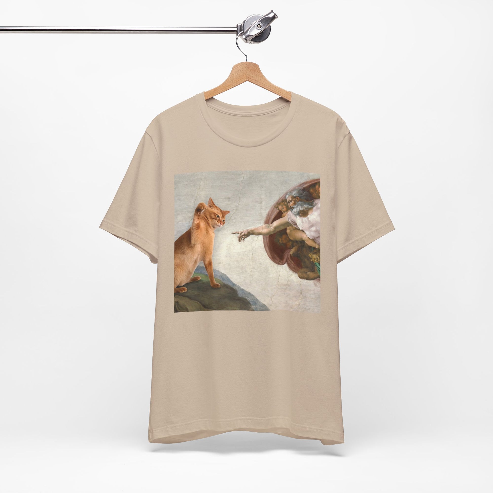 Beige t-shirt with a graphic design of a cat and angel on a hanger against a white background