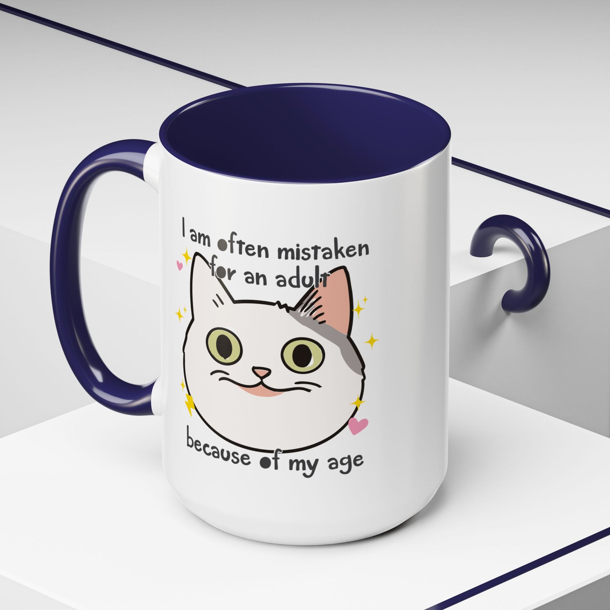 White ceramic mug with purple handle and interior featuring a cute wide-eyed cat face, hearts, sparkles, and the phrase “I am often mistaken for an adult because of my age.”
