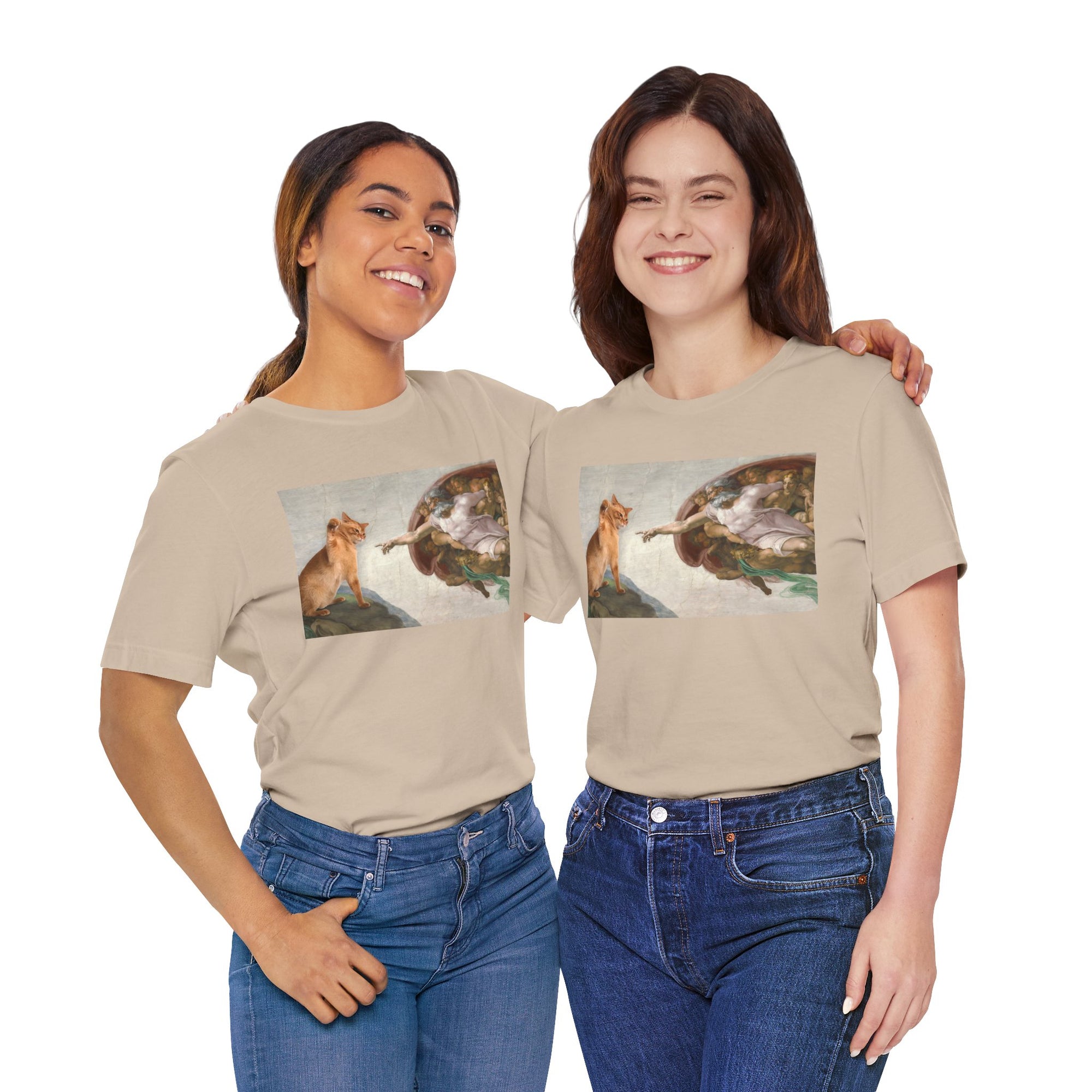 Two women wearing matching beige t-shirts with a graphic design of a cat and god.