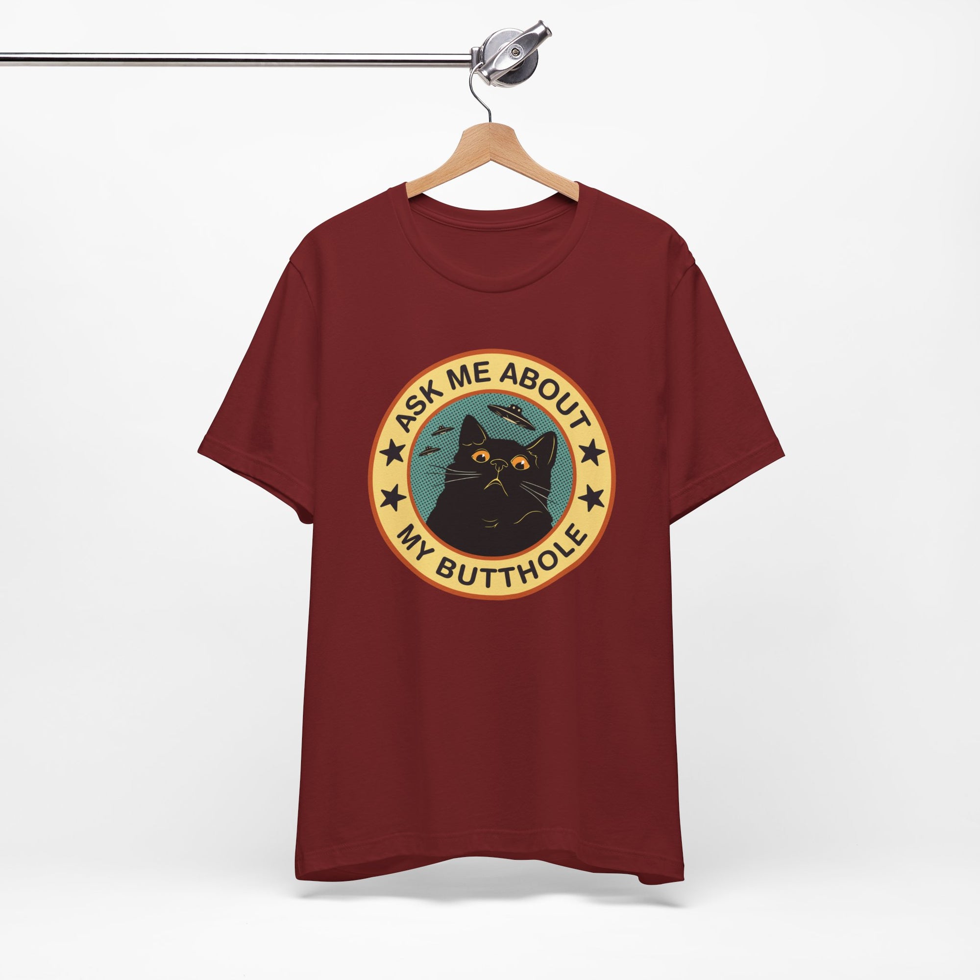 Maroon t-shirt with a graphic design of a cat and text on a hanger against a white background