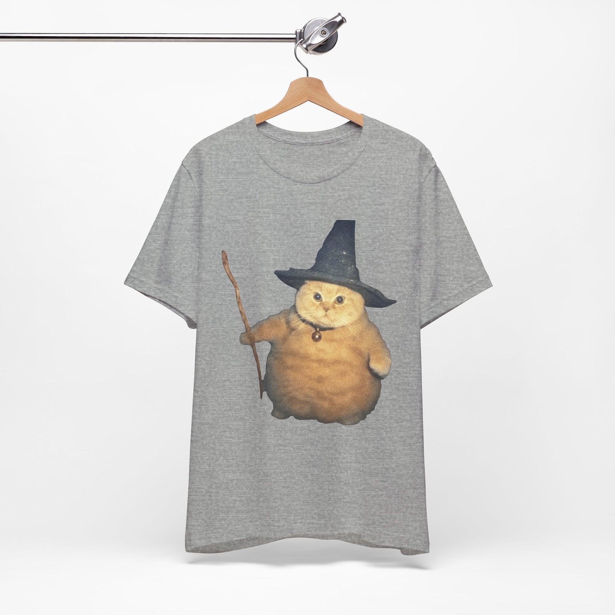 Gray t-shirt with a cat wearing a witch hat and broomstick graphic on a hanger.