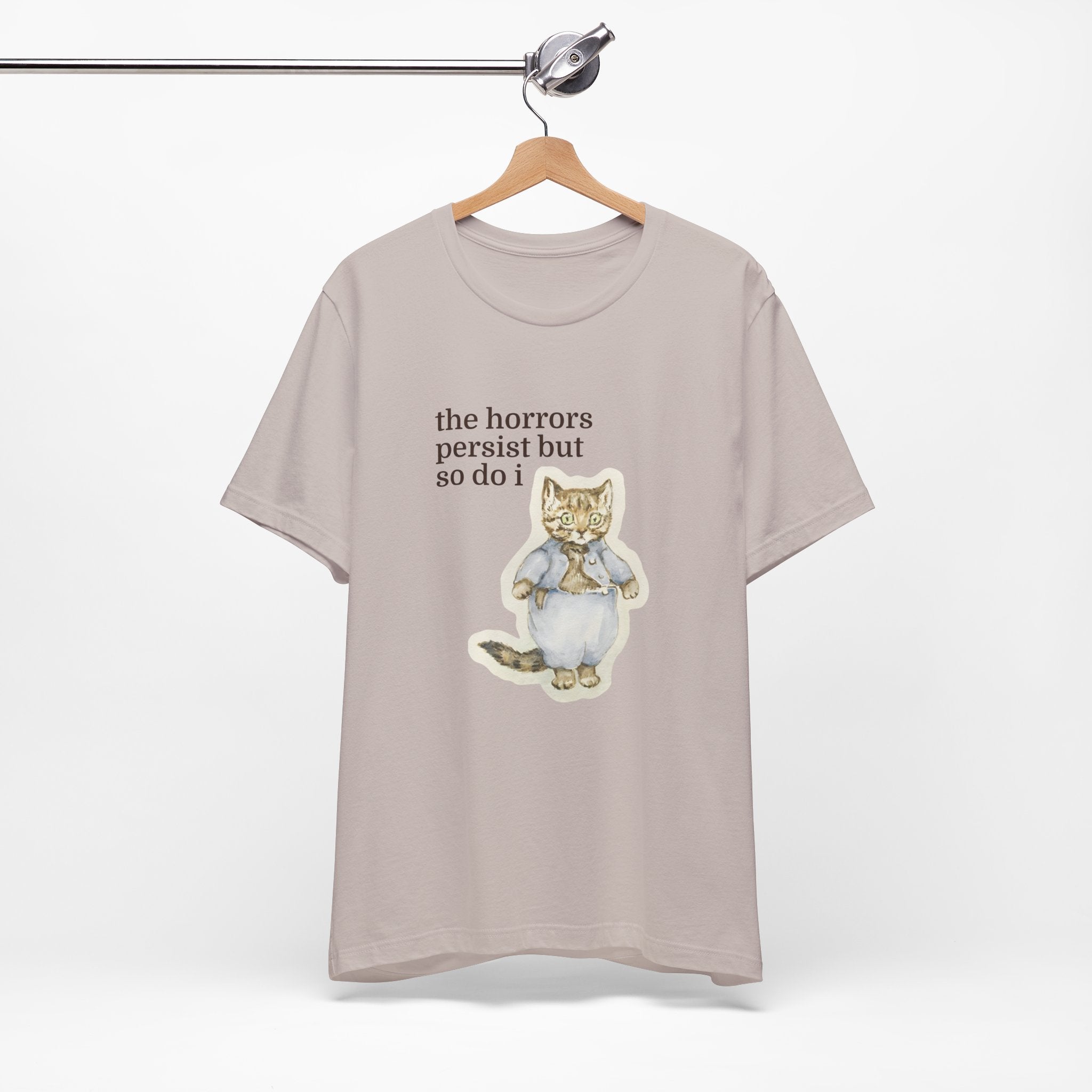 Beige t-shirt featuring a vintage-style illustrated cat in blue clothing with the phrase “the horrors persist but so do i.”