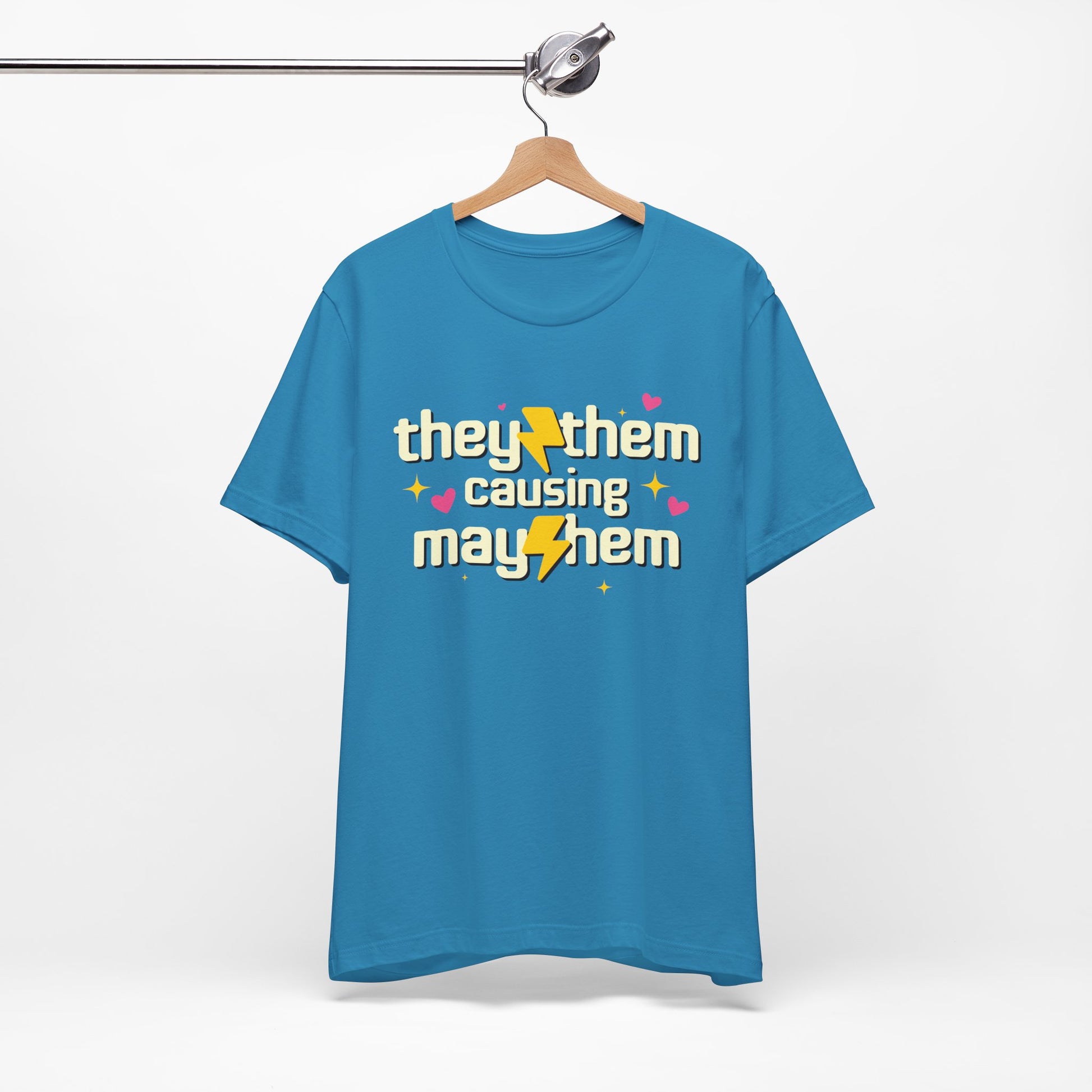 Blue t-shirt with 'they/them causing mayhem' text on a hanger against a white background