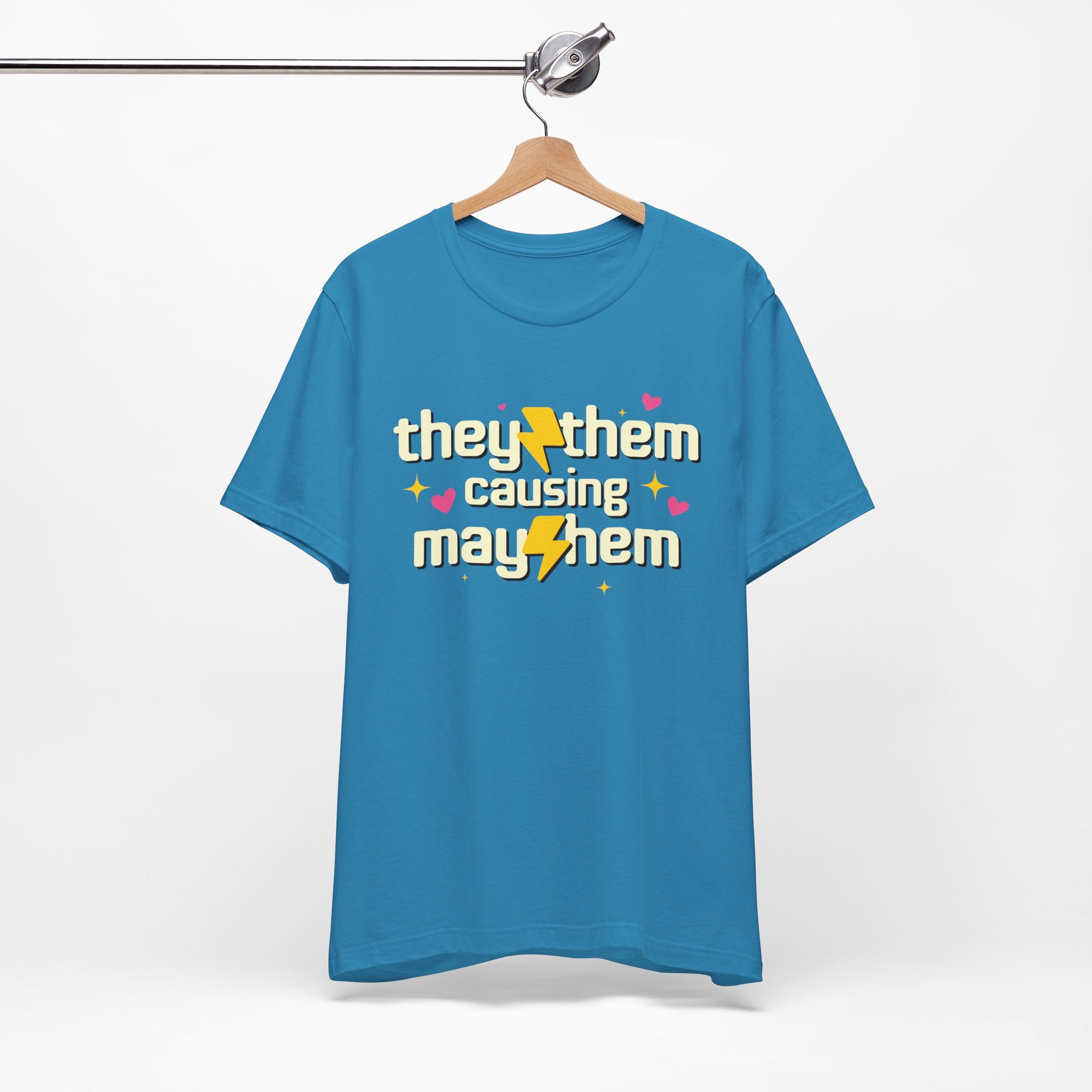 Blue t-shirt with 'they/them causing mayhem' text on a hanger against a white background