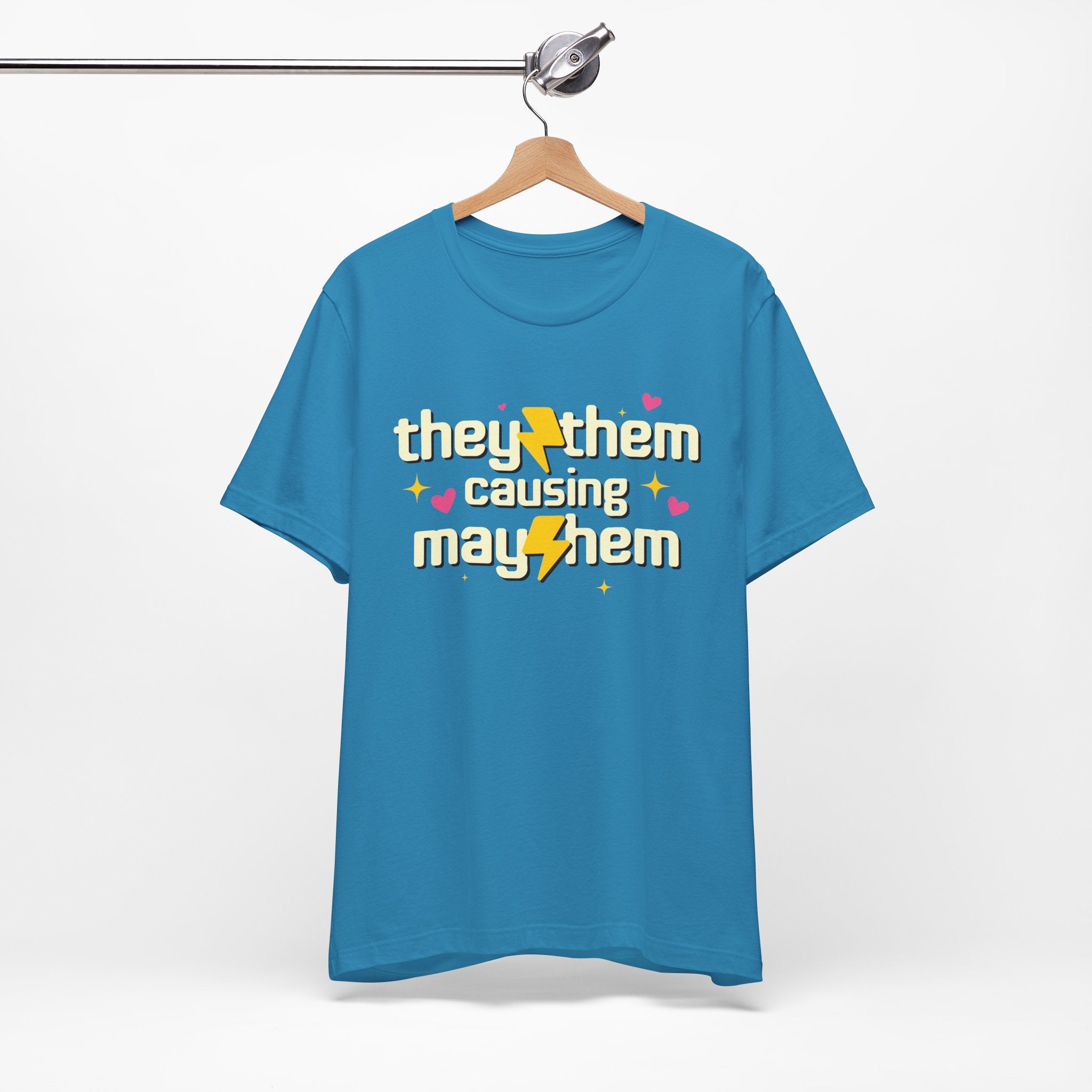 Blue t-shirt with 'they/them causing mayhem' text on a hanger against a white background