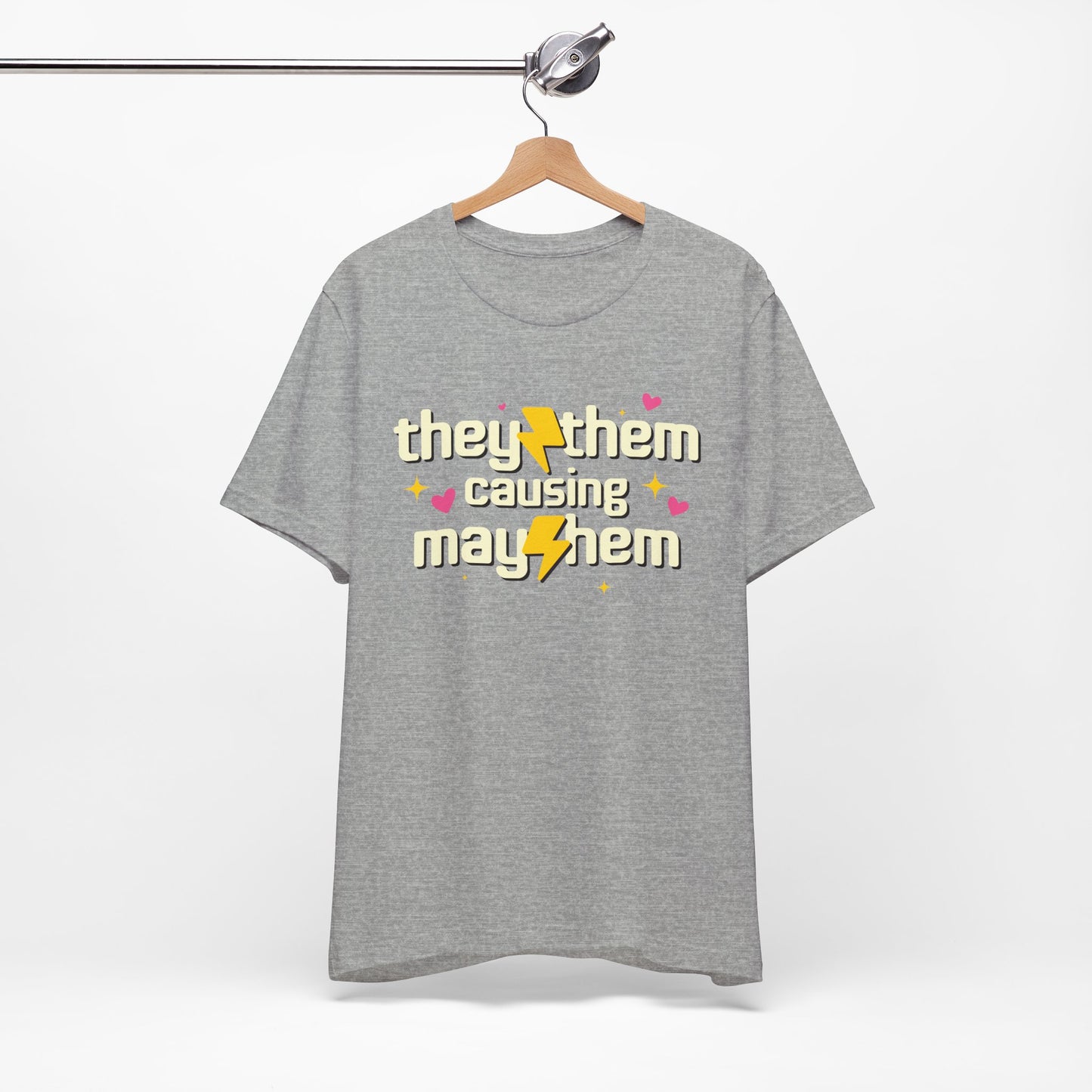 Gray t-shirt with 'they/them causing mayhem' text on a hanger against a white background
