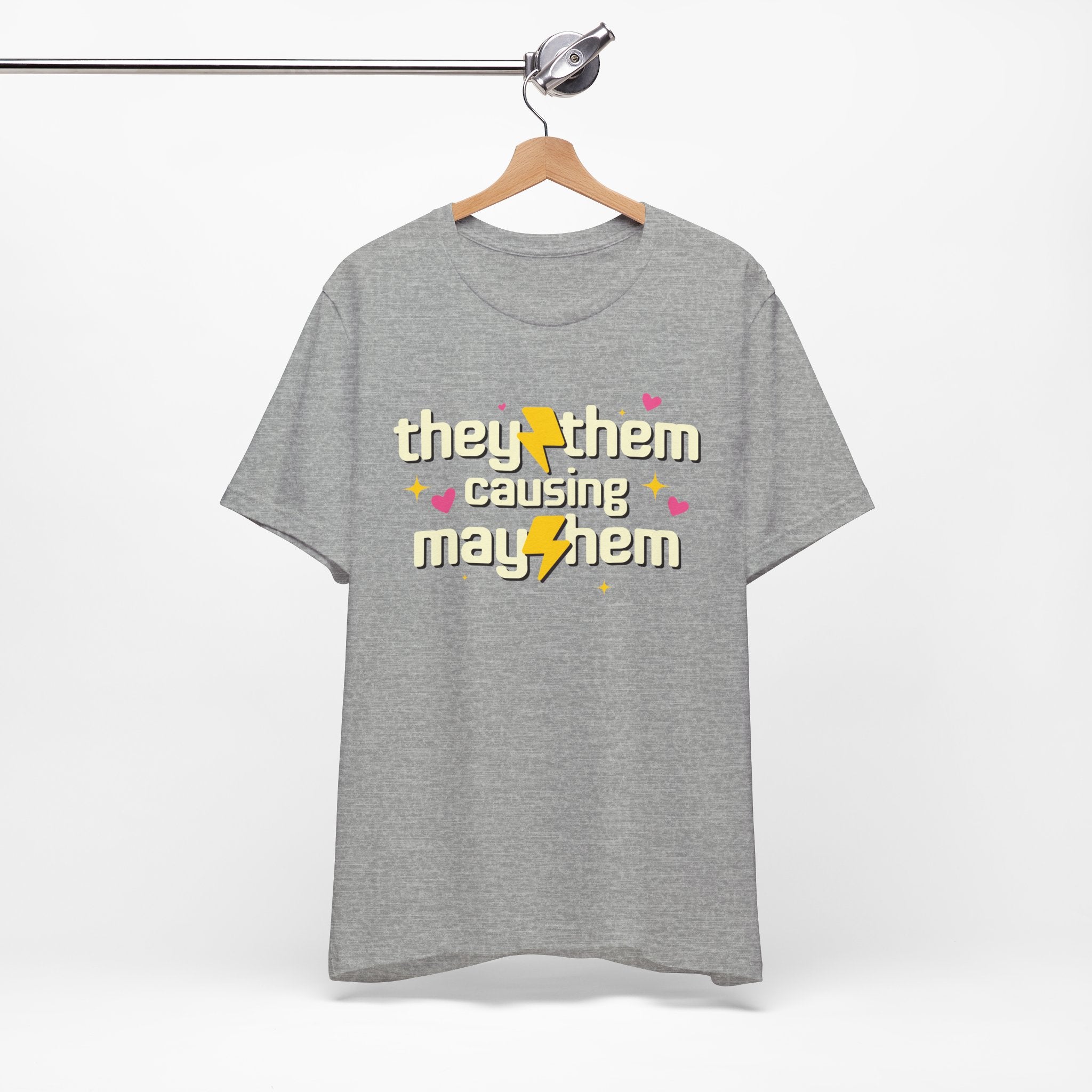 Gray t-shirt with 'they/them causing mayhem' text on a hanger against a white background