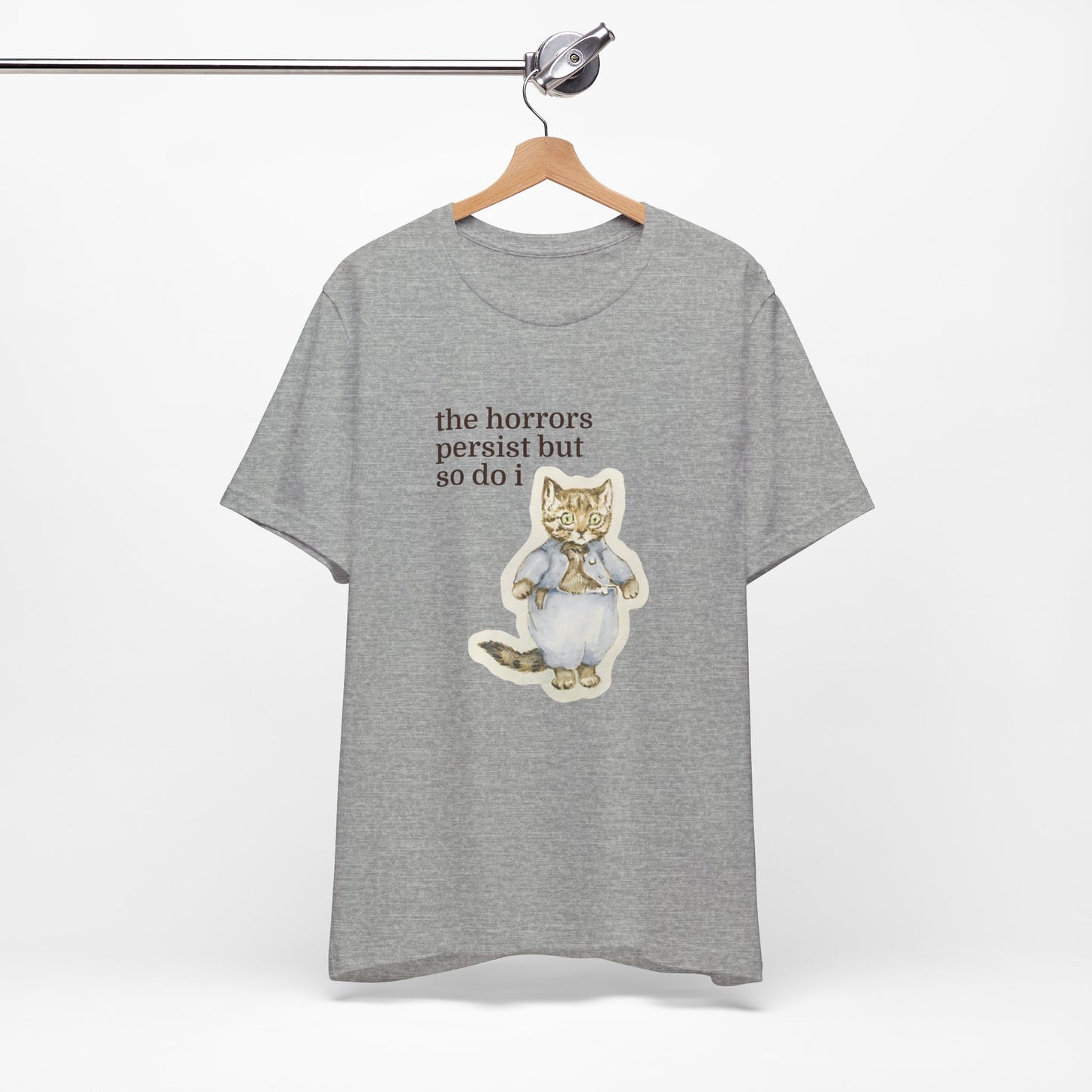 Grey t-shirt featuring a vintage-style illustrated cat in blue clothing with the phrase “the horrors persist but so do i.”