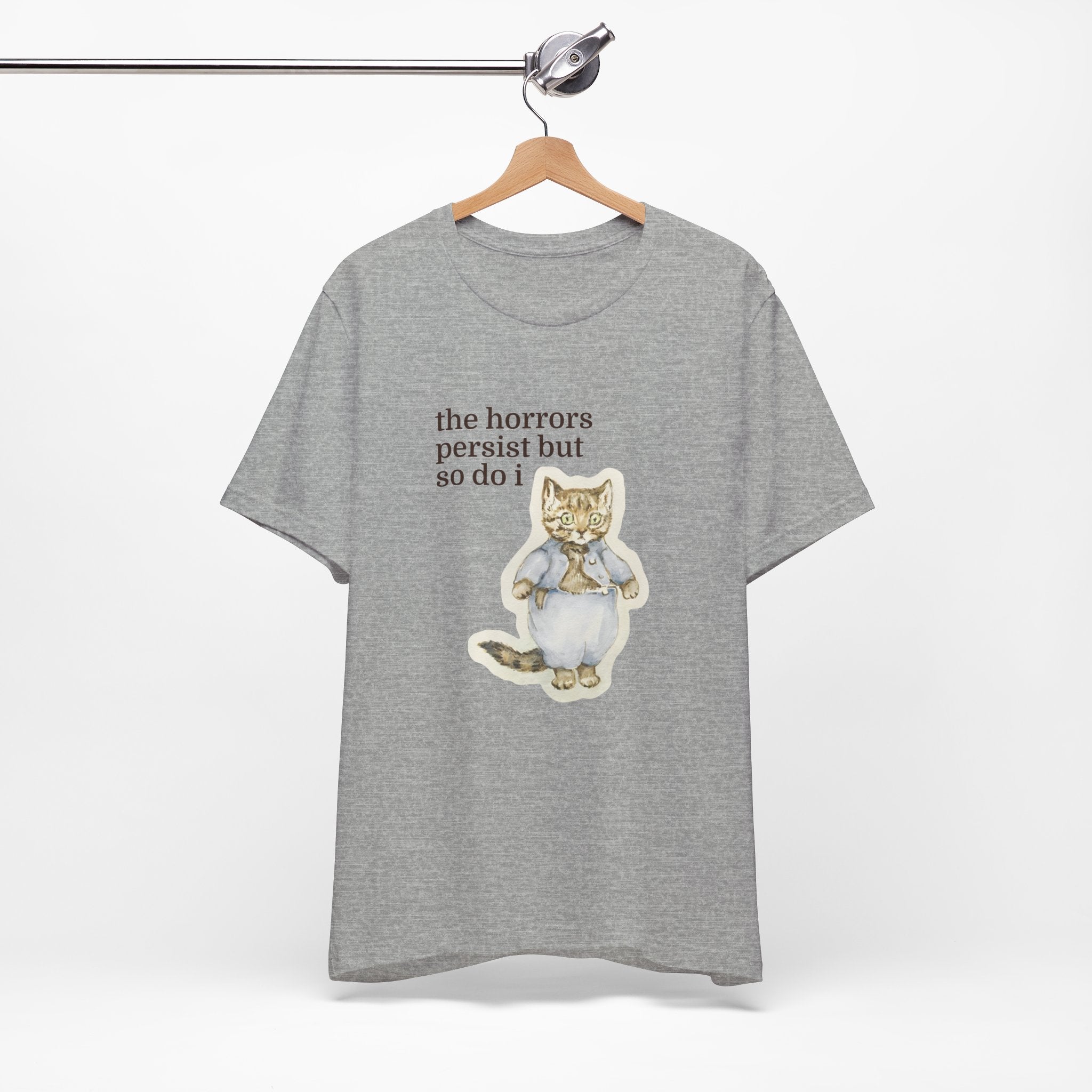 Grey t-shirt featuring a vintage-style illustrated cat in blue clothing with the phrase “the horrors persist but so do i.”