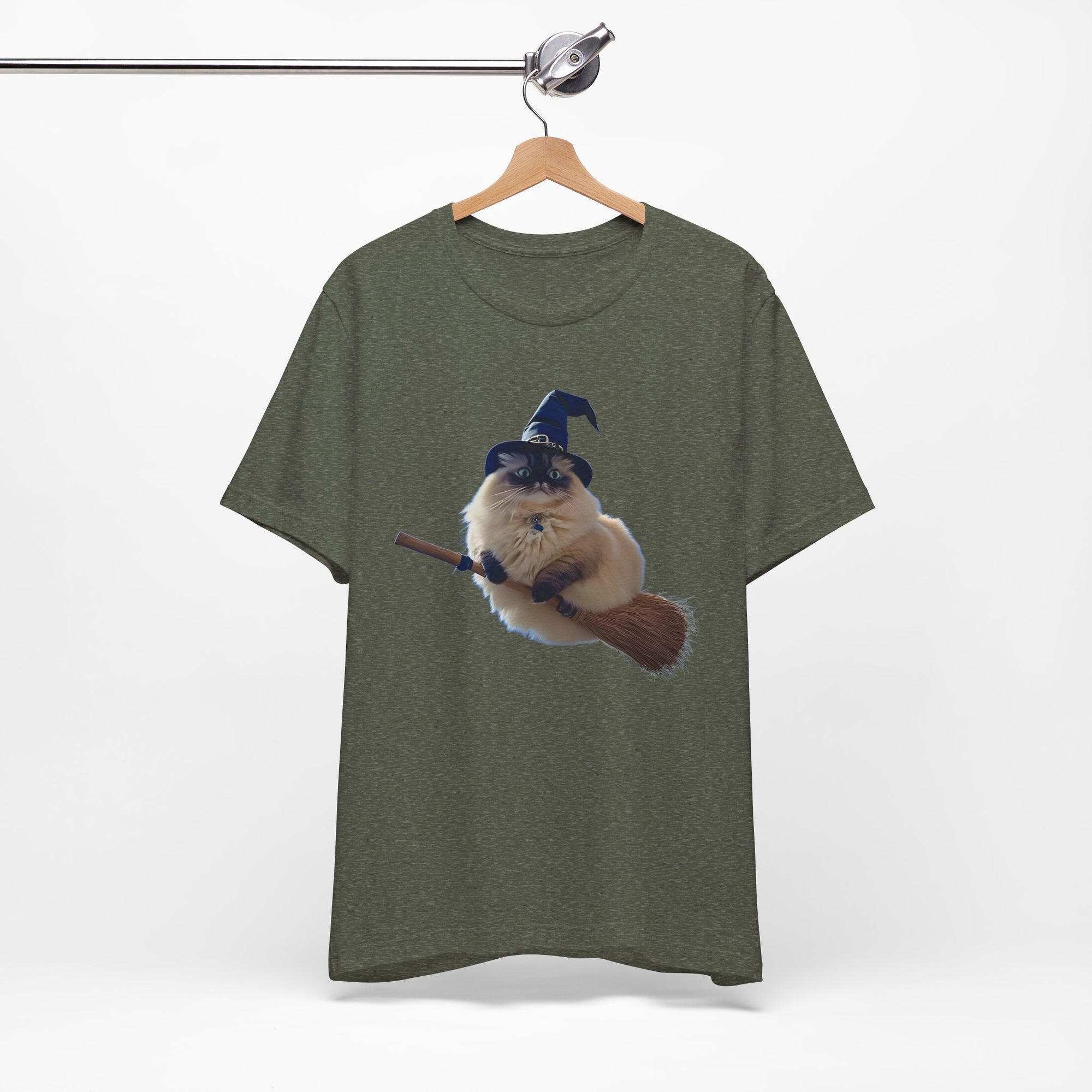 Green t-shirt with a graphic of a cat in a witch hat and broomstick on a hanger against a white background