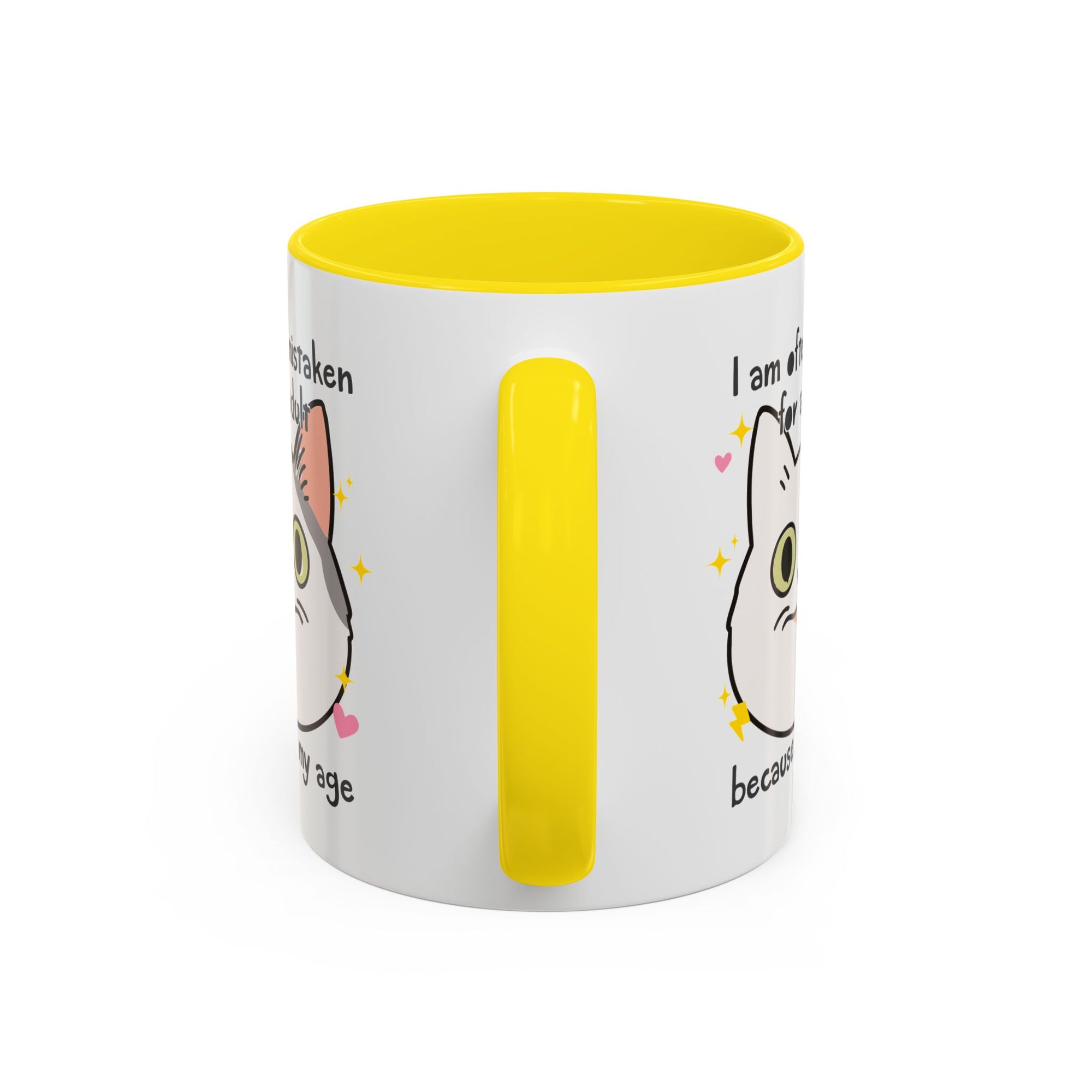 White ceramic mug with yellow handle and interior featuring a cute wide-eyed cat face, hearts, sparkles, and the phrase “I am often mistaken for an adult because of my age.”
