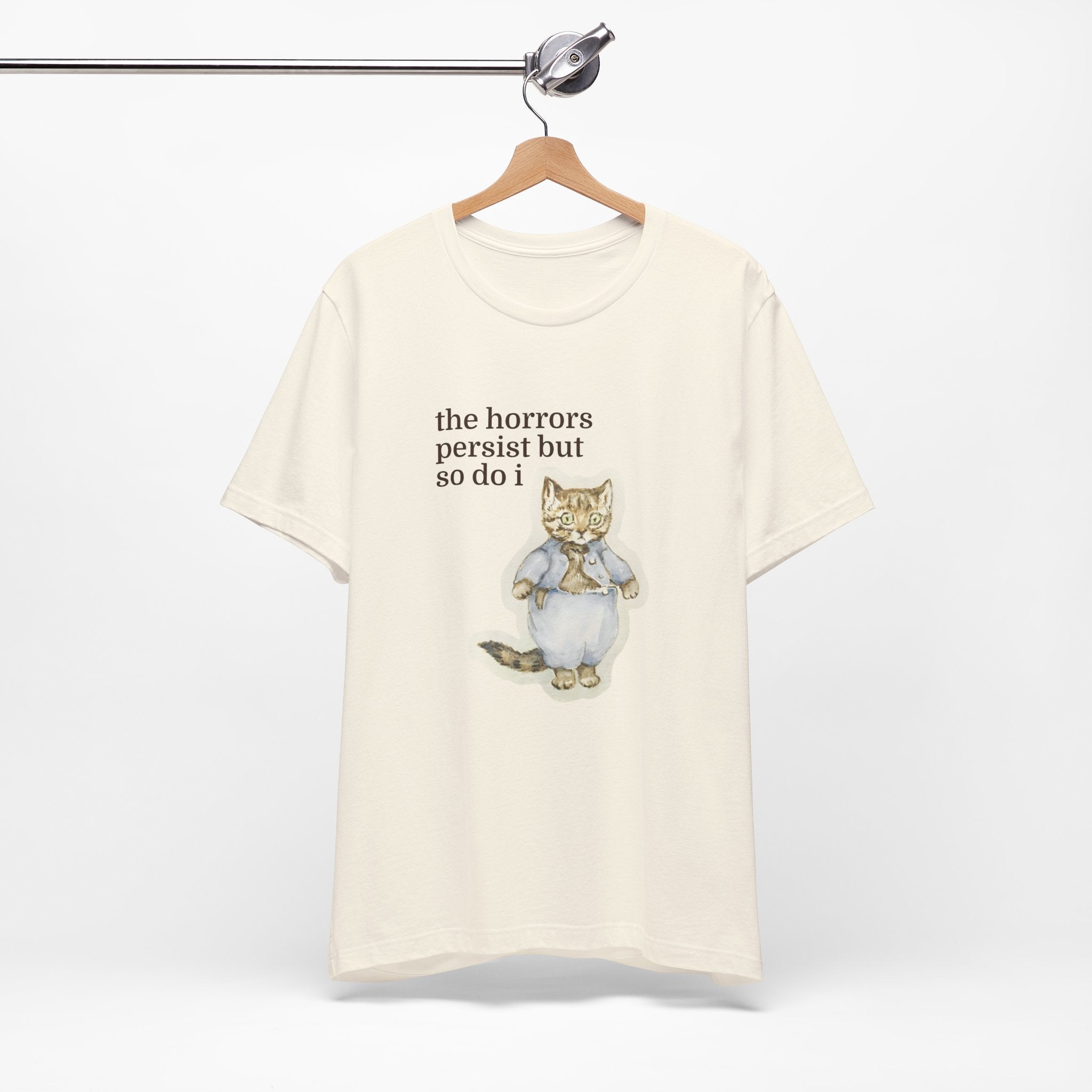 White t-shirt featuring a vintage-style illustrated cat in blue clothing with the phrase “the horrors persist but so do i.”