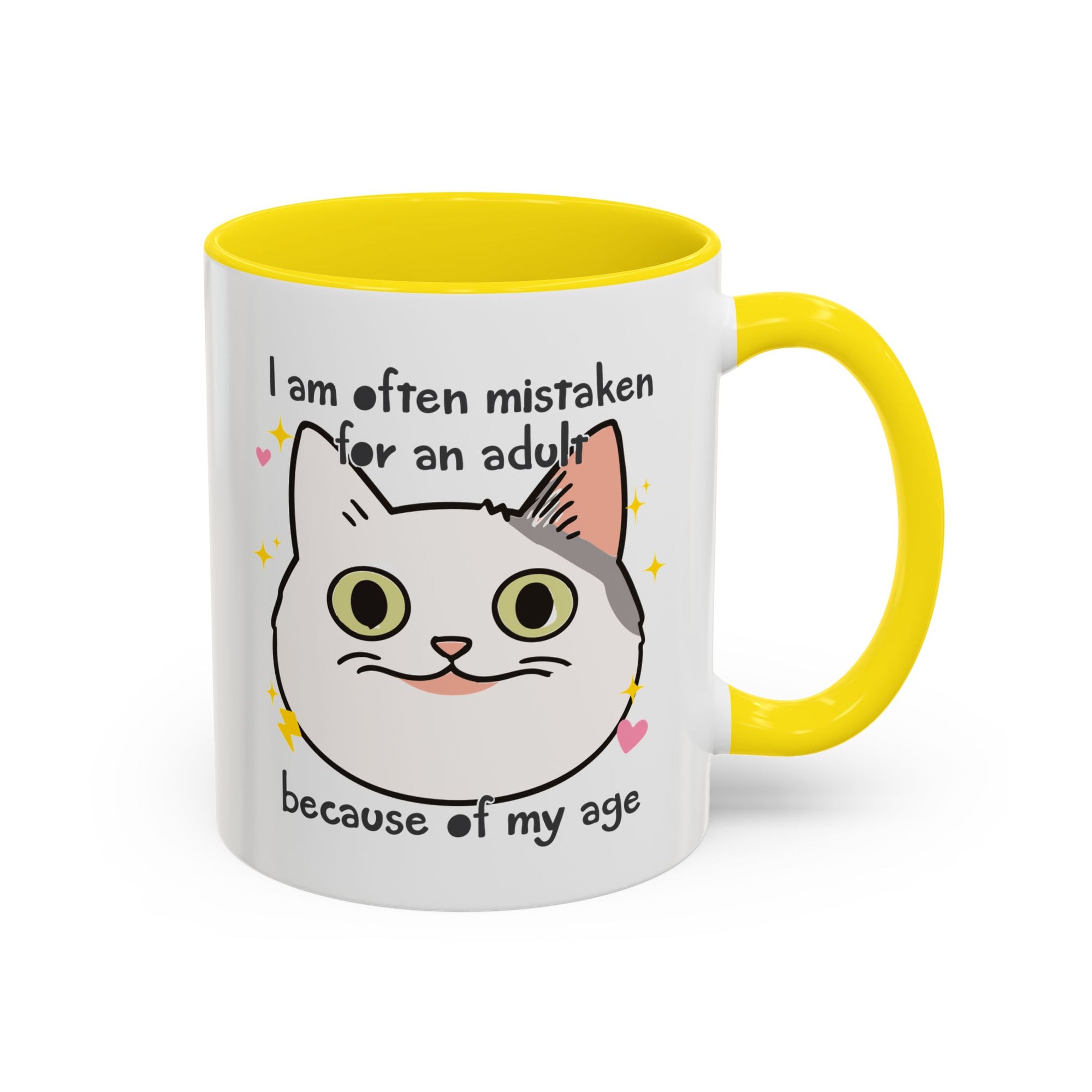 White ceramic mug with yellow  handle and interior featuring a cute wide-eyed cat face, hearts, sparkles, and the phrase “I am often mistaken for an adult because of my age.”
