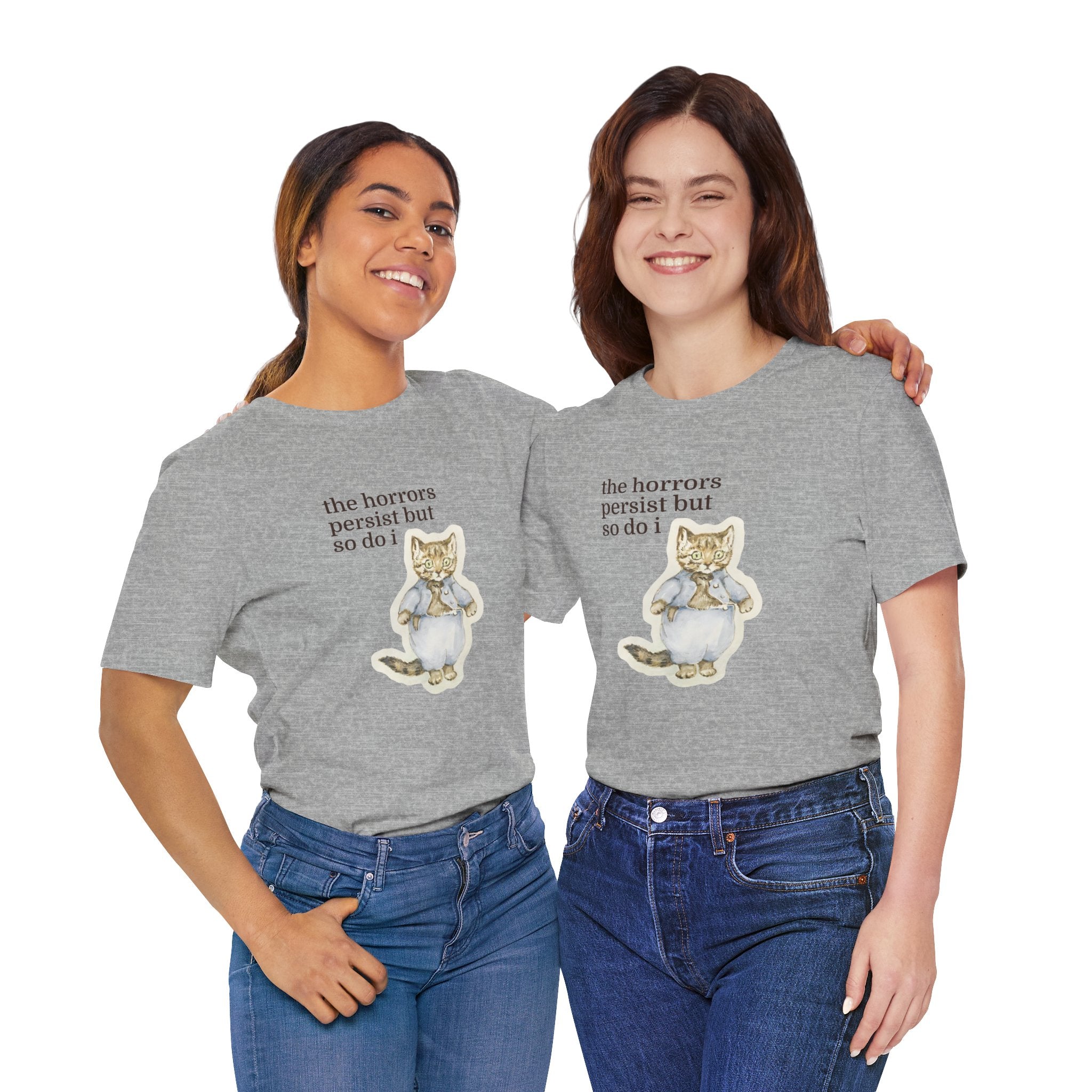 Two people wearing gray t-shirt featuring a vintage-style illustrated cat in blue clothing with the phrase “the horrors persist but so do i.”