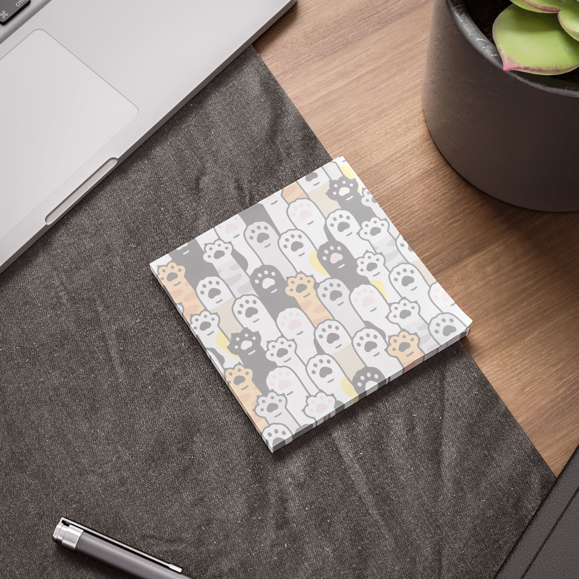 Post it notes with cat paws with cat pattern on a desk next to a laptop and plant