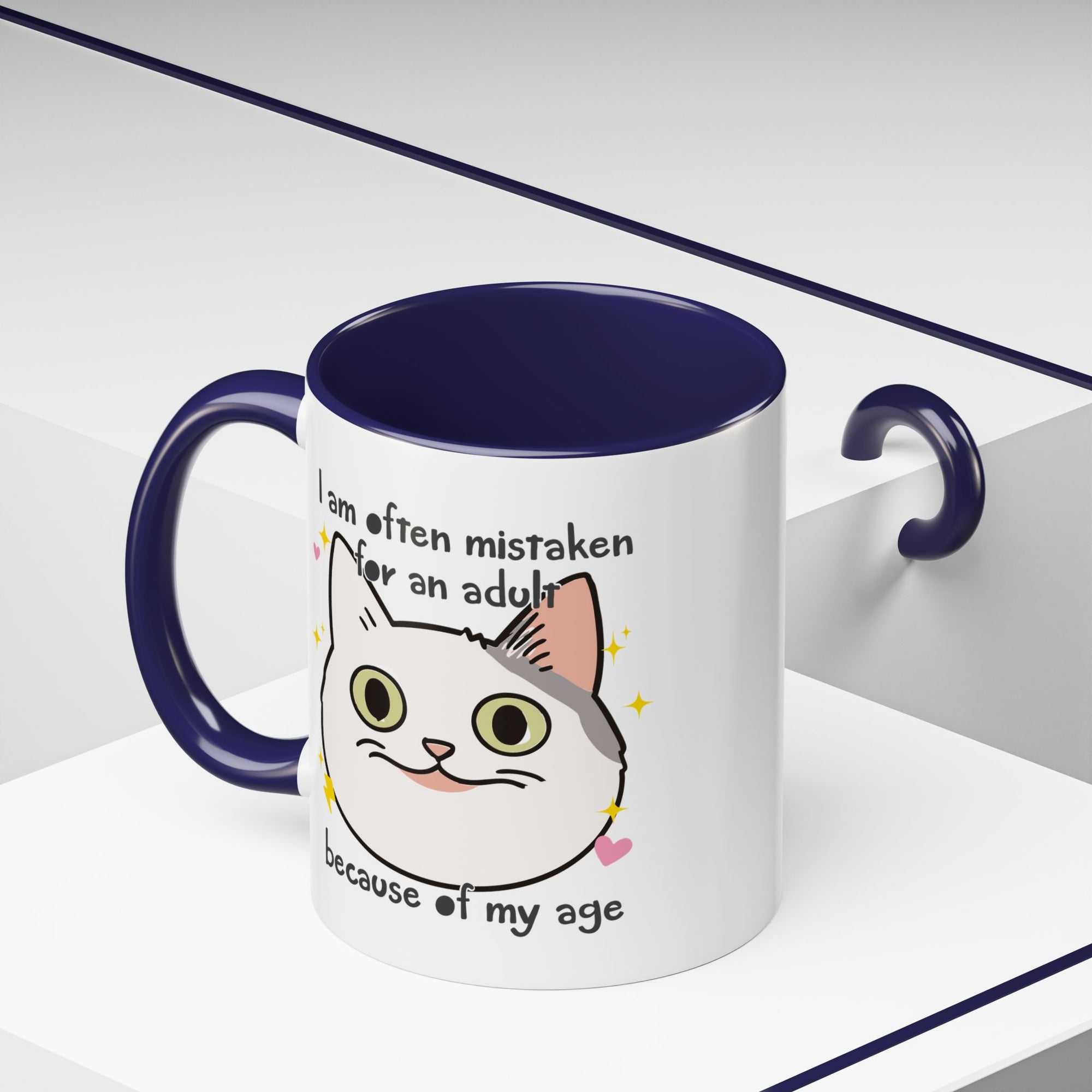 White ceramic mug with purple handle and interior featuring a cute wide-eyed cat face, hearts, sparkles, and the phrase “I am often mistaken for an adult because of my age.”

