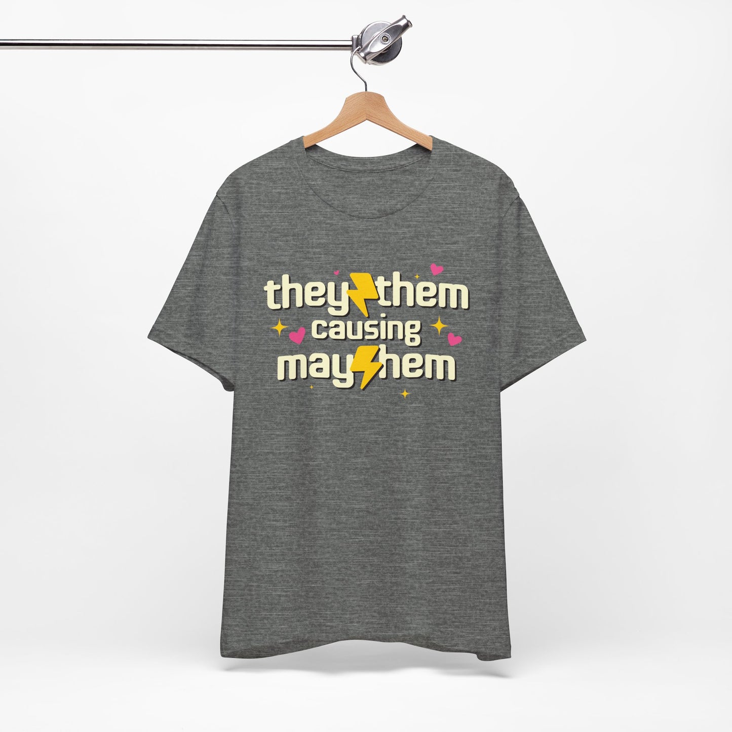 Gray t-shirt with 'they/them causing mayhem' text on a hanger against a white background