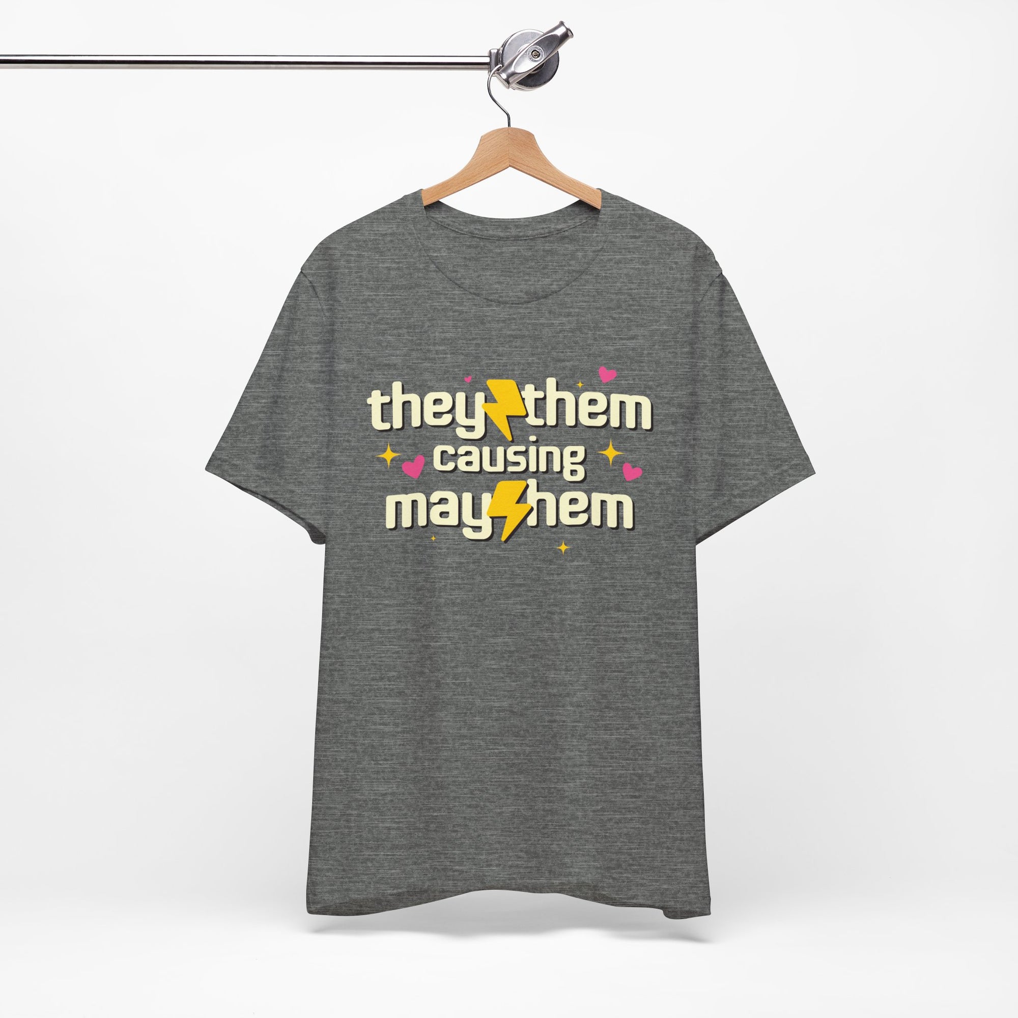 Gray t-shirt with 'they/them causing mayhem' text on a hanger against a white background